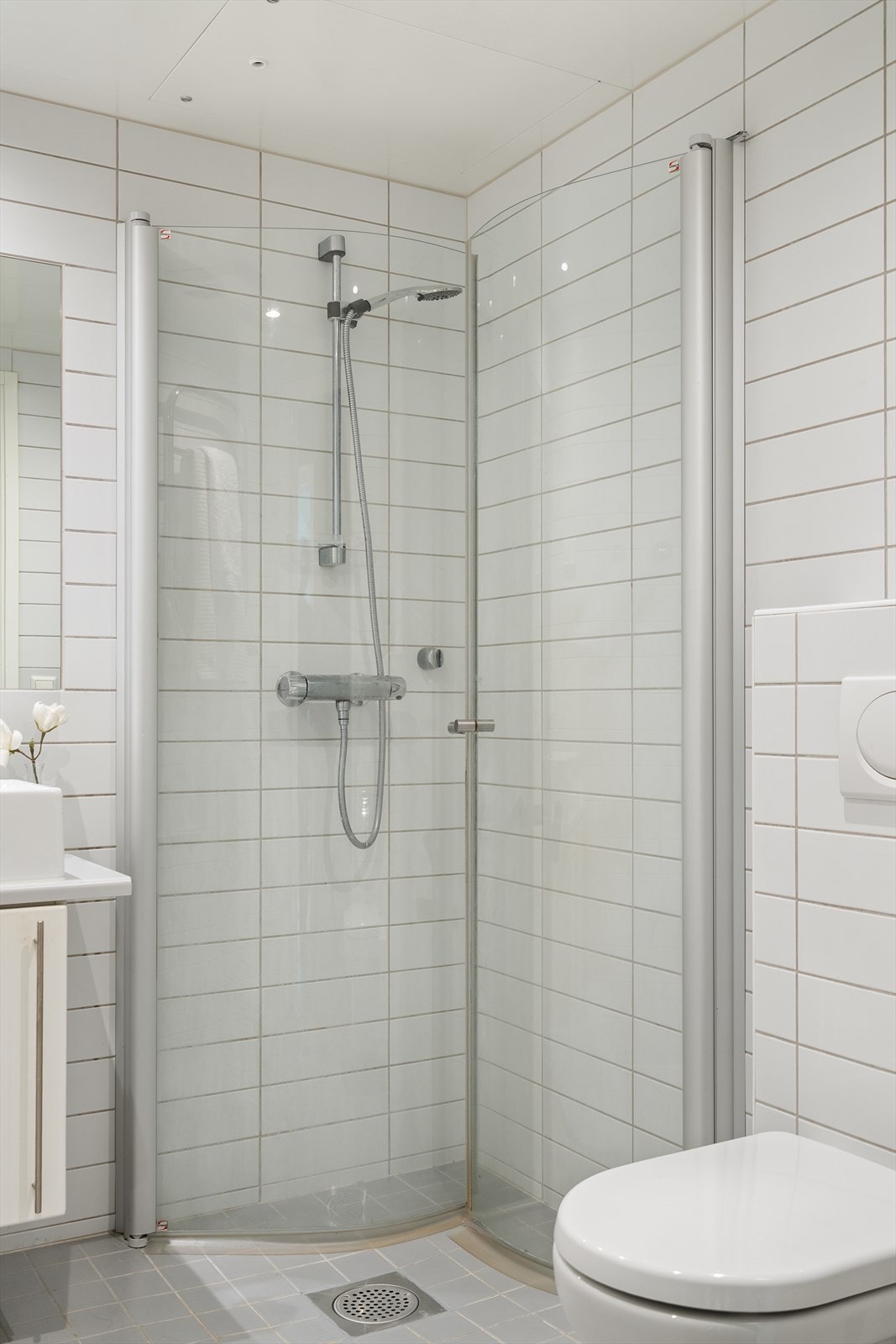 Her finner du dusjløsning med glassdører, veggmontert toalett, servant med underskap, speil og håndkletørker. Galleribilde