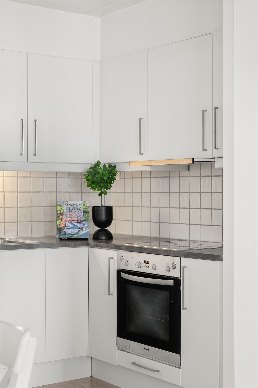 Kjøkkenet er utstyrt med integrerte hvitevarer som stekeovn, platetopp, oppvaskmaskin og kjøl/frys. Den lyse fargepaletten og de tidløse flisene over benk gir rommet et stilrent uttrykk som lett lar seg kombinere med ulike interiørvalg. Galleribilde