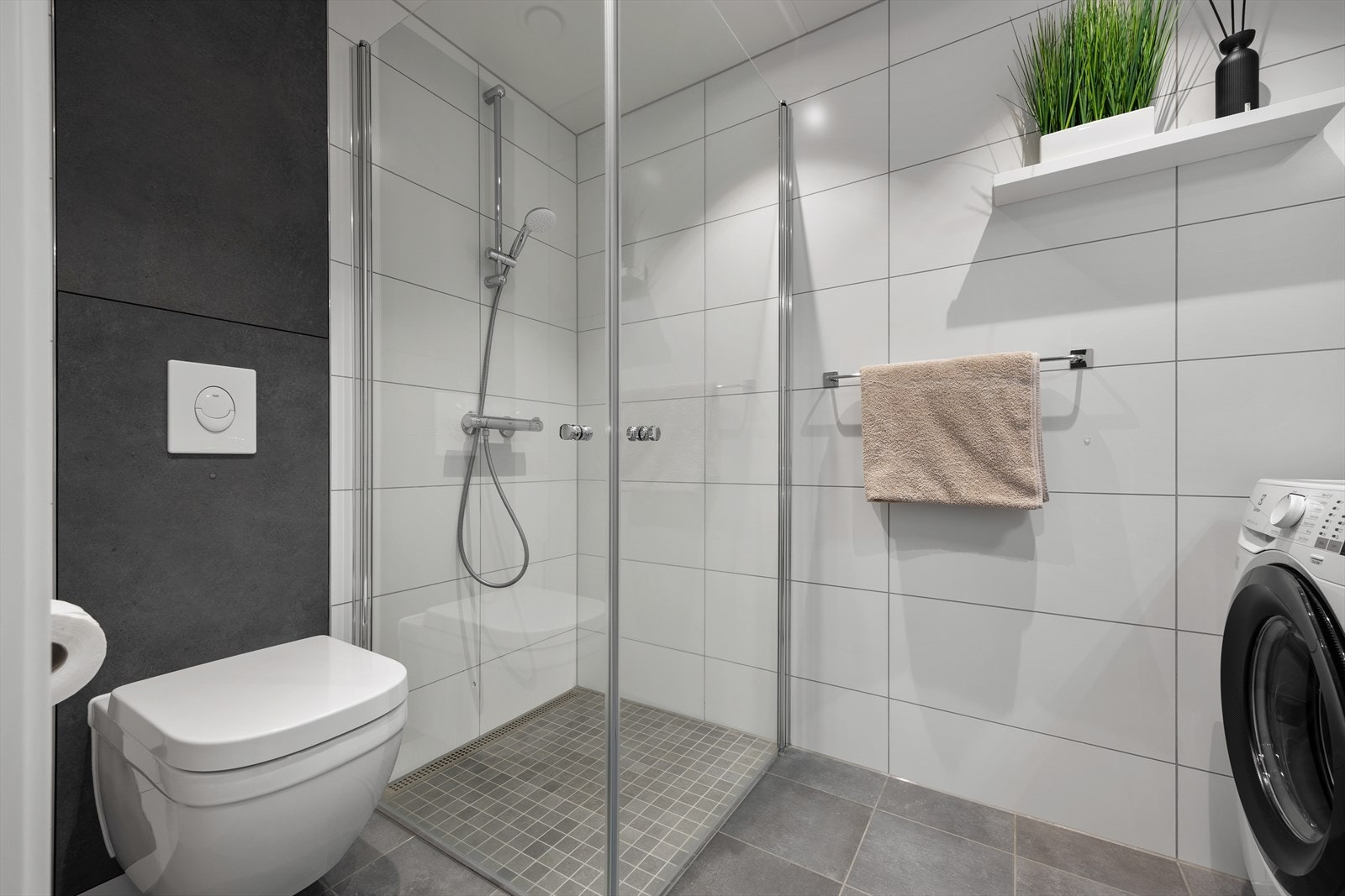 Badet er utstyrt med dusjhjørne med innfellbare glassvegger, vegghengt wc og servantinnredning med skuffer og overskap. Galleribilde