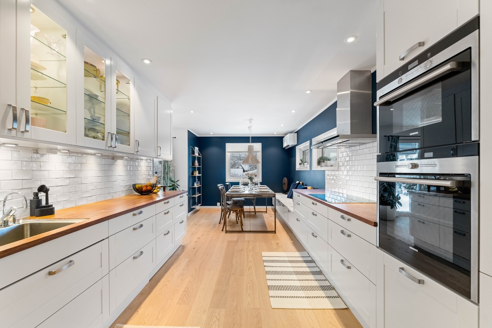 Rommet er naturlig delt inn i to soner: en funksjonell kjøkkendel for matlaging og en hyggelig spisestuesone markert med en elegant mørk blå kontrastvegg. Galleribilde