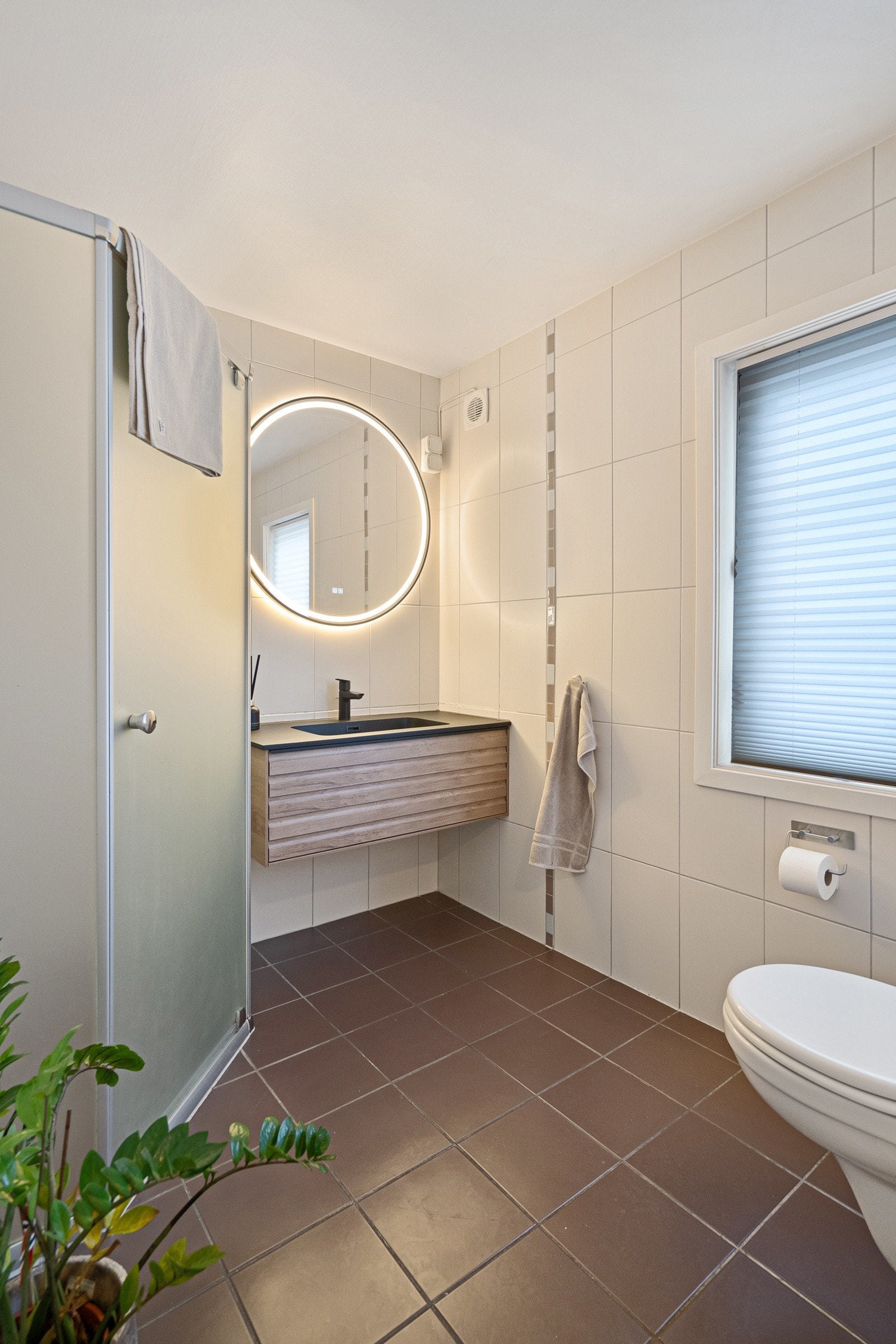 Badet i 1. etasje er flislagt og har varmekabler i gulv. Rommet er utstyrt med servant, veggmontert toalett og dusj, og har en praktisk og funksjonell utforming. Galleribilde