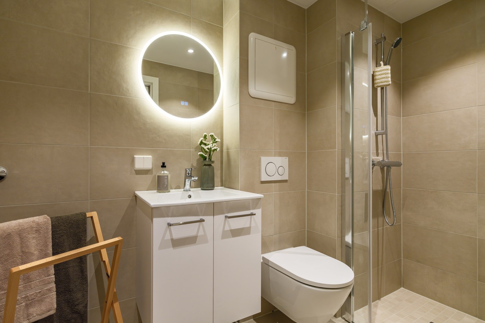 Lekkert flislagt bad fra 2025 med vegghengt toalett, dusj, baderomsinnredning og opplegg for vaskemaskin Galleribilde