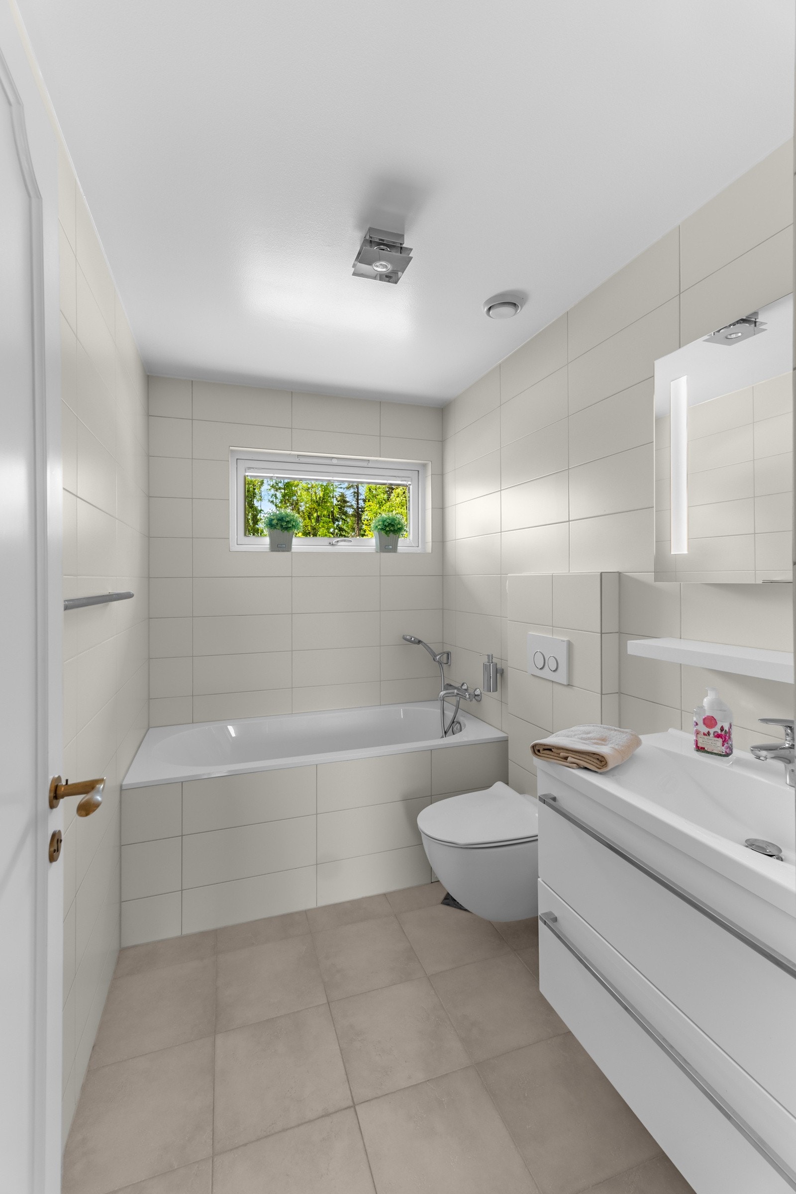 Innbydende baderom med lyse fliser og komfortabelt badekar Galleribilde