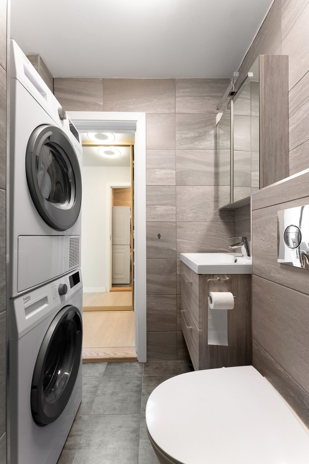 Badet er innredet med dusjnisje med veggmontert regn- og hånddusj, helservant, speilskap med lys og vegghengt toalett Galleribilde