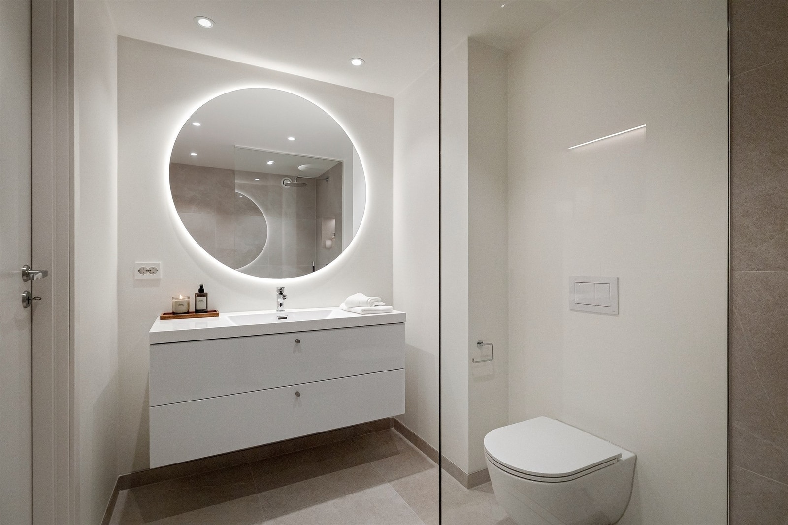 Badene har flislagte overflater i kombinasjon med slette vegger med integrert nisjer. Vegghengt toalett, baderomsinnredning og regnfallsdusj Galleribilde