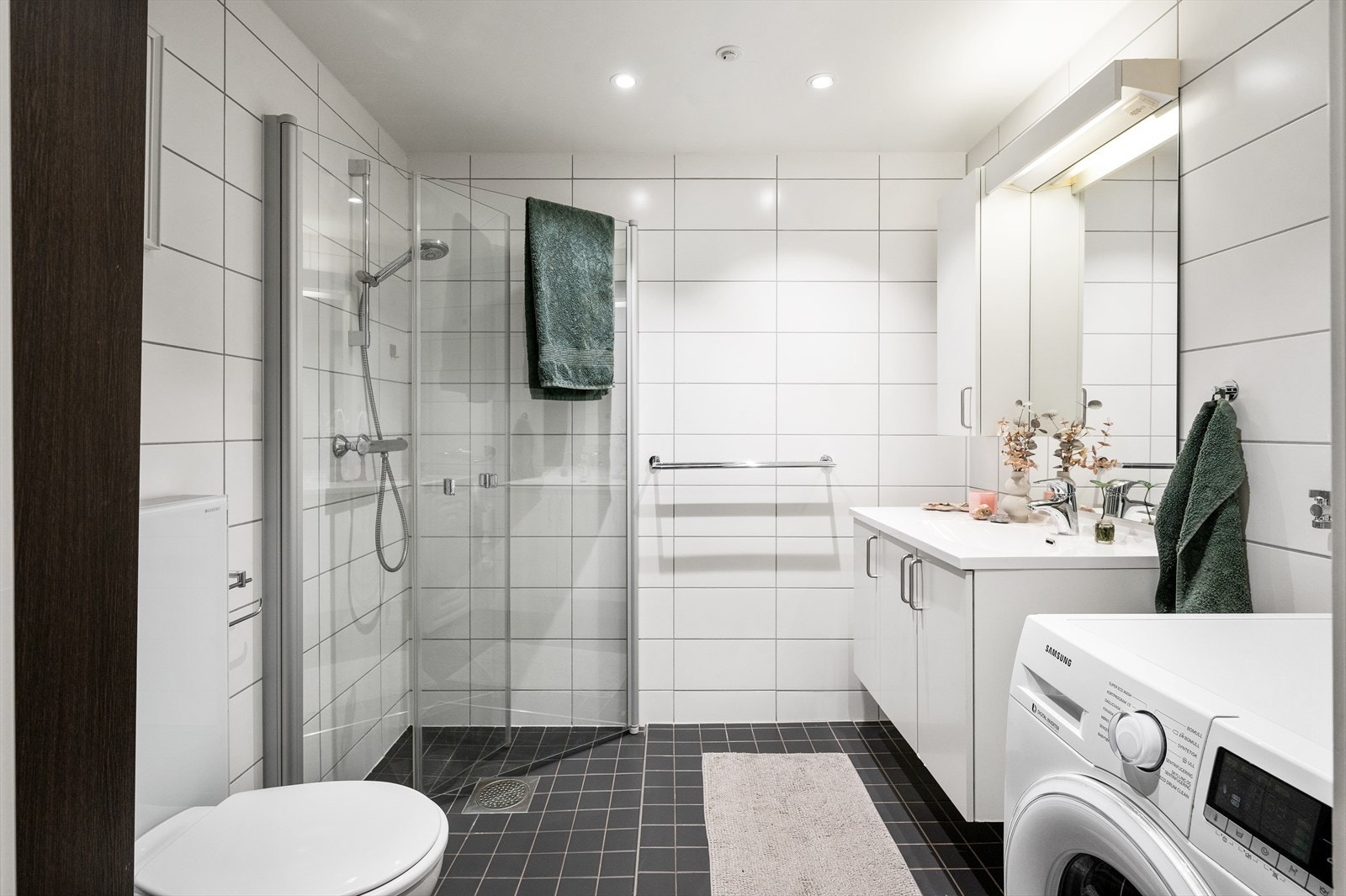 Badet er innredet med vegghengt toalett, servant nedfelt i praktisk innredning, speilskap med integrert lys, samt dusjhjørne med svingbare glassdører. Galleribilde