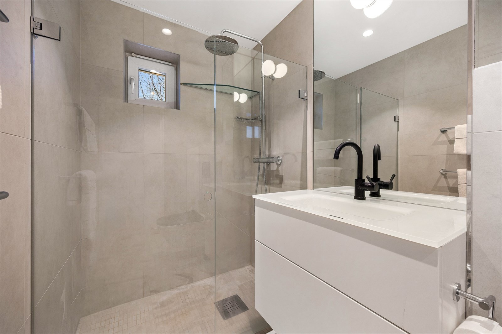 Romslig dusjnisje med glassdører, regnfallsdusj og moderne, sorte armaturer. Galleribilde