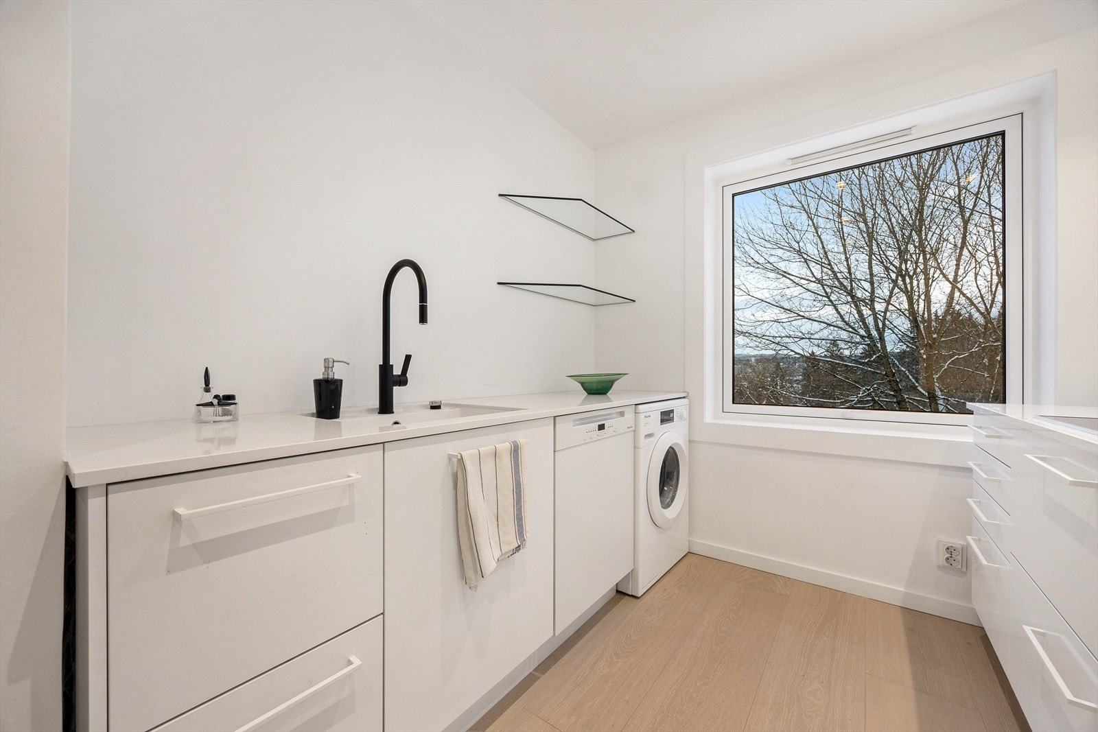 Her er det opplegg for vaskemaskin, og benkeplaten i komposittstein er både slitesterk og stilren. Galleribilde