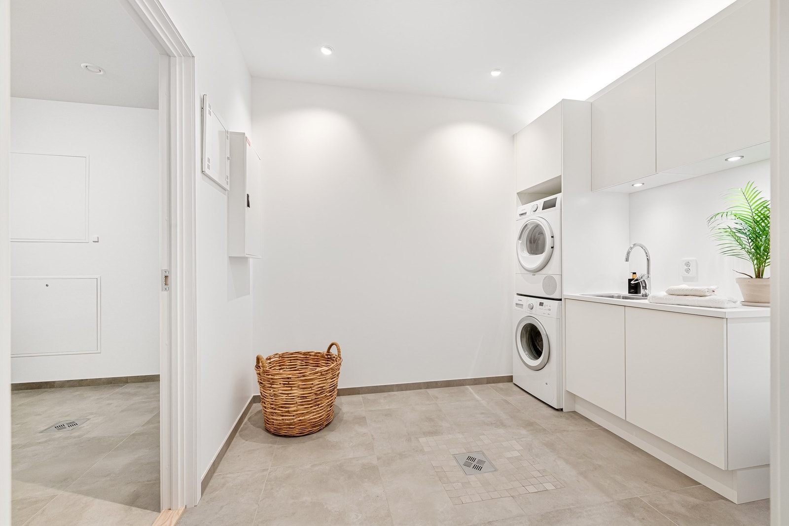 Vaskerom med romslig innredning fra HTH med hvite glatte fronter og god oppbevaringsplass. Benkeplate av laminat med nedfelt skyllekum med ett-greps armatur. Opplegg for vaskemaskin og tørketrommel. Galleribilde