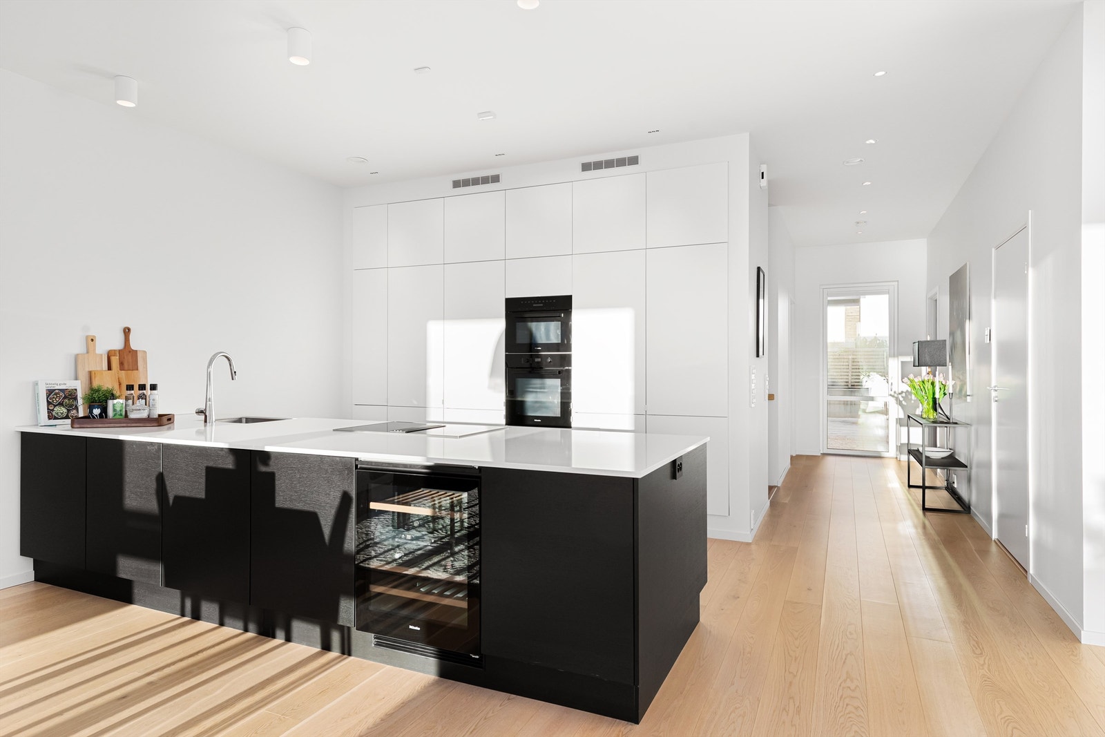 Kjøkkeninnredning fra HTH med hvite fronter på høyskap og mørke glatte fronter på kjøkkenøy. Benkeplate av stein Galleribilde