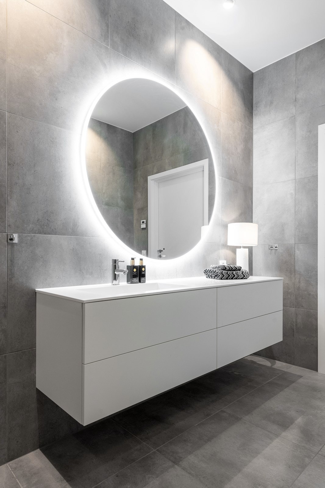 Stor romslig baderomsinnredning fra Azzurro med hvite glatte fronter og nedfelt vask med ett-greps armatur. Rundt speil med lys og stikkontakter over servant. Galleribilde