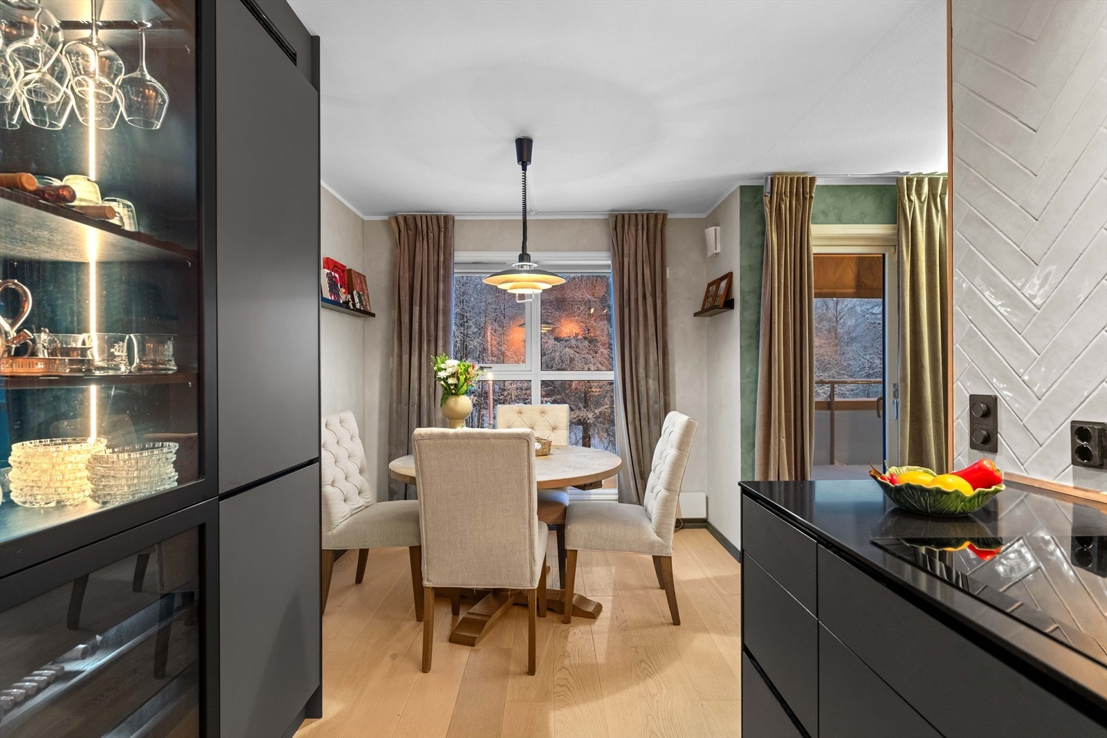 Her får man et flott, velutstyrt kjøkken, med funksjonelle detaljer som Quooker kran (3 liter) og innfelt belysning i et stilig vitrineskap. Veggene er kledd med lekre, lysegrå fliser i fiskebensmønster. Galleribilde