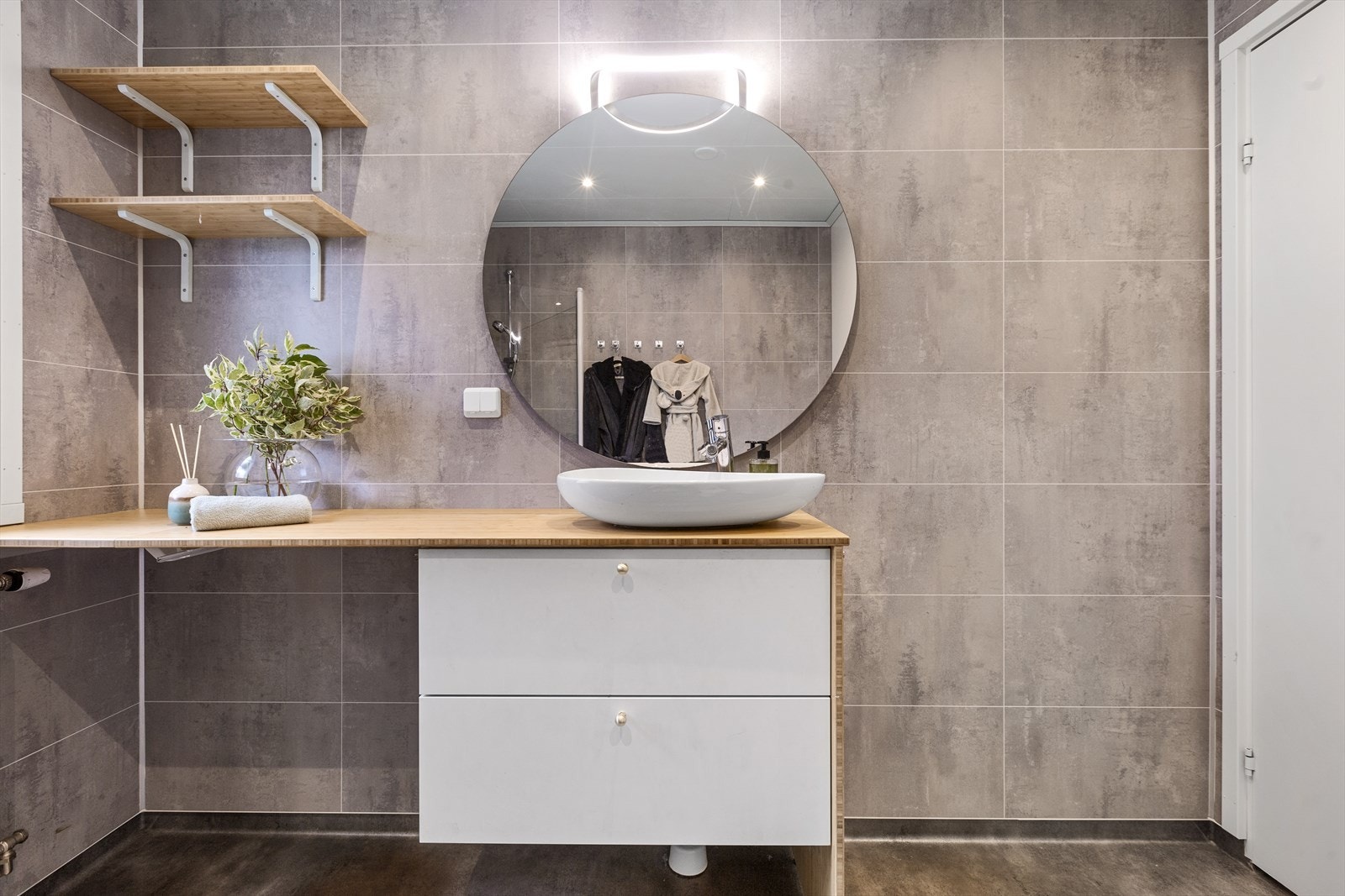 Videre er rommet utstyrt med baderomsinnredning med servant, dusjhjørne med innfellbare dører og toalett. Det er elektriske varmekabler i gulvet og ventilasjon via mekanisk avtrekk. Galleribilde