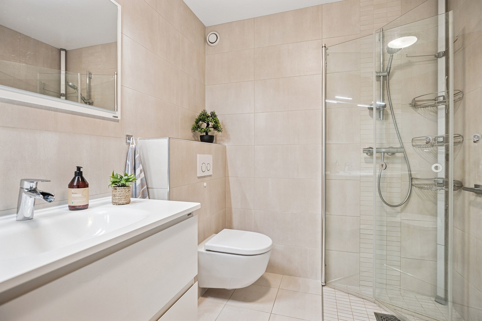 Badet har moderne servantinnredning, vegghengt toalett og dusjhjørne med innfellbare glassdører. Galleribilde