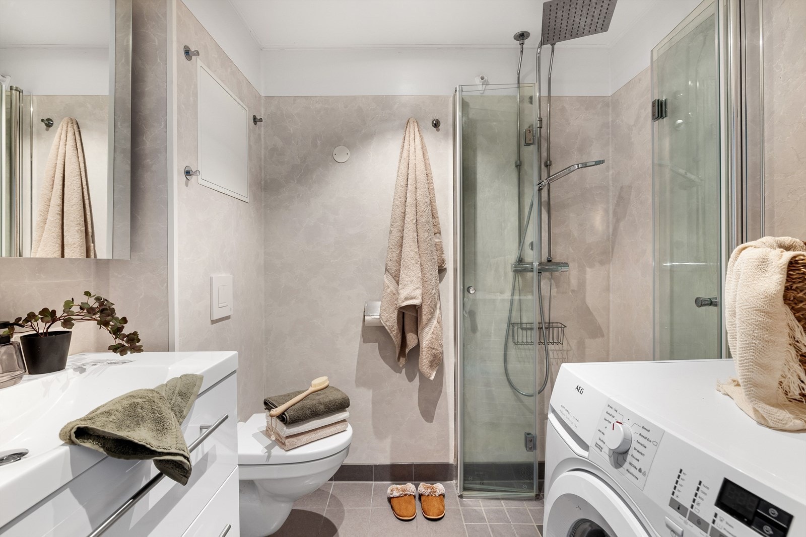 Videre inn på badet blir vi møtt med en moderne innredning. Her er det nytt flislagt gulv fra 2024 med varmekabler, regnfallsdusj med Gustavsberg-armatur og leddede dusj-dører fra Viking Bad. Galleribilde