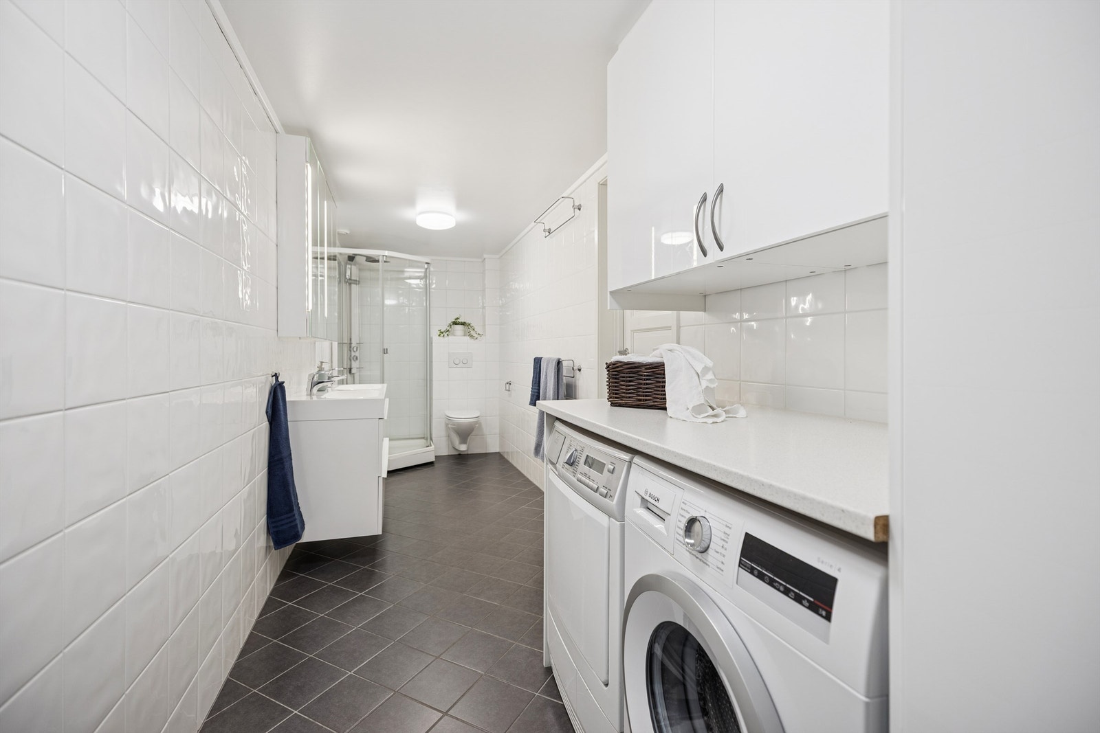 Pent flislagt bad/vaskerom i underetasjen med dobbel servantinnredning, dusjkabinett, vegghengt toalett og opplegg for vaskemaskin og tørketrommel. Galleribilde
