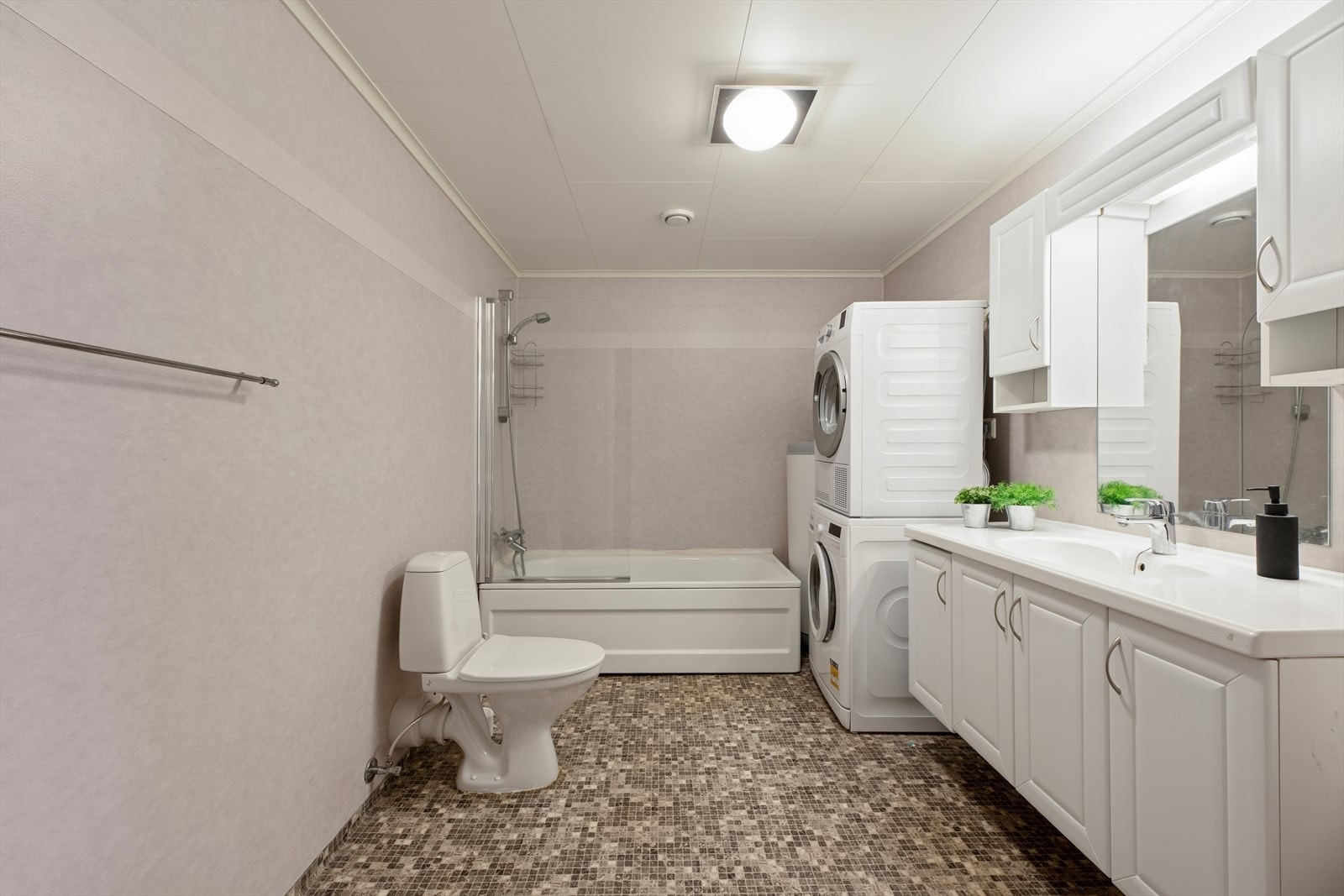 Romslig baderom med servant med skapinnredning, gulvmontert toalett, badekar med dusj og opplegg til vaskemaskin. Galleribilde