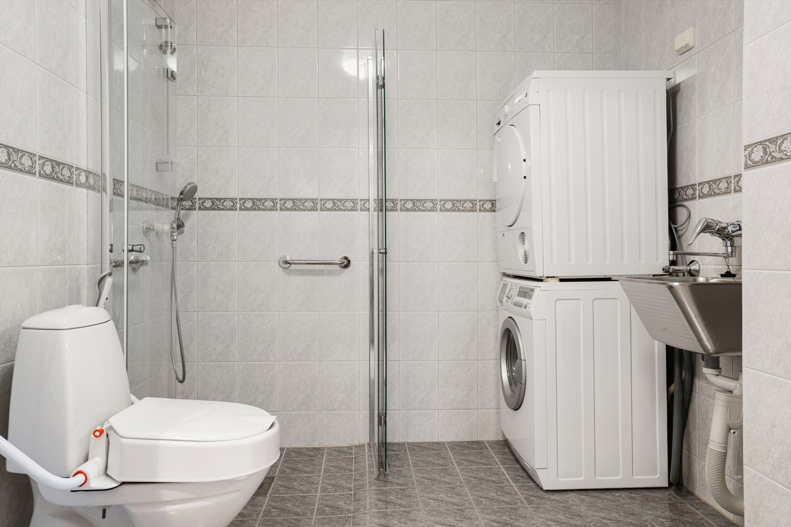 Rommet er innredet med en baderomsinnredning med nedfelt servant, toalett, dusjhjørne, utslagsvask og opplegg for vaskemaskin/tørketrommel. Galleribilde