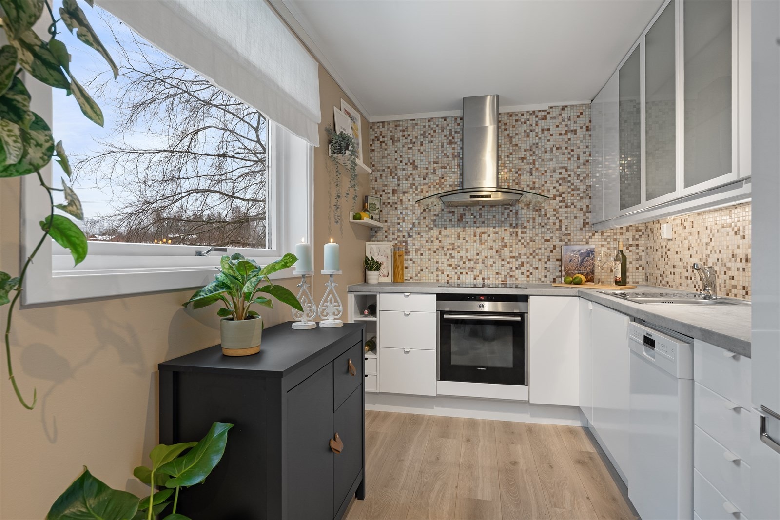 Lyst kjøkken med komfyr, inductionstopp, oppvaskmaskin og ventilator med avtrekk ut. Galleribilde