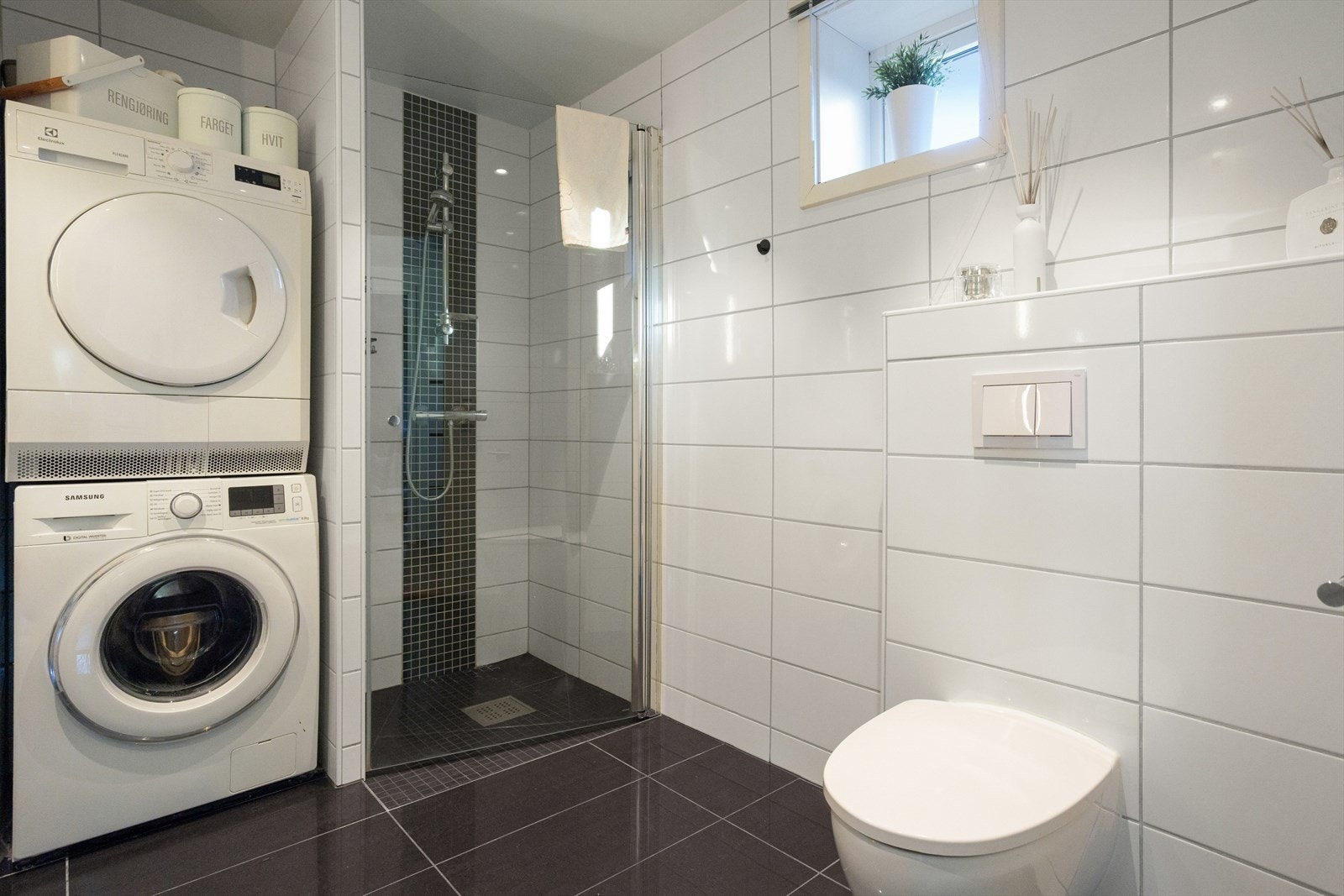 Badet er helfliset og innredet med dusjnisje med glassdør, vegghengt toalett og opplegg for vaskemaskin og tørketrommel. Galleribilde