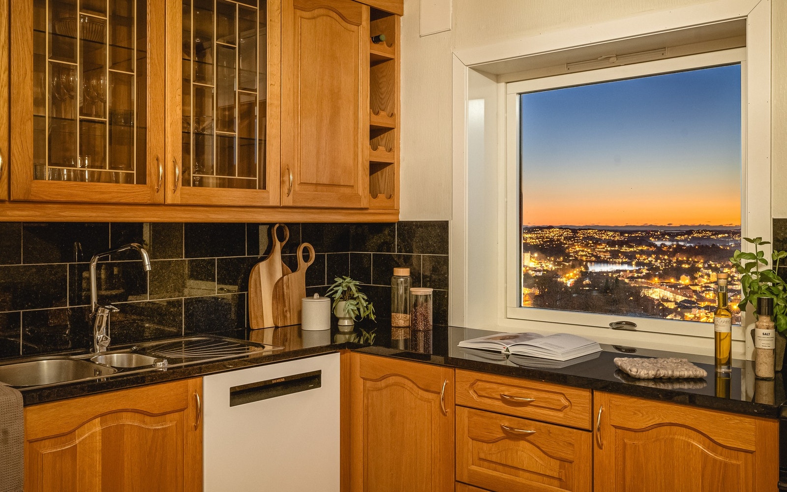 Kjøkkeninnredningen består av profilerte fronter, ett overskap har glassfront, benkeplate i stein, over benkeplaten er det benyttet fliser, stål oppvaskkum og ventilator. Galleribilde