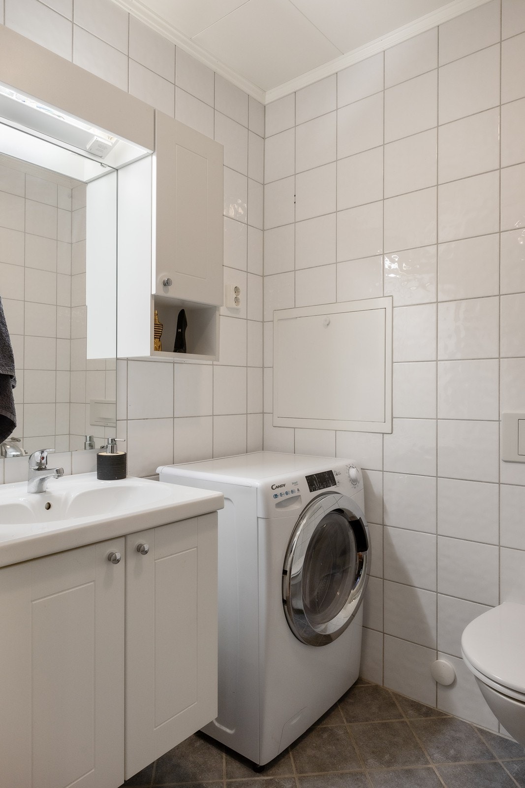 Innredningen har heldekkende servant over skapseksjon, matchende veggskap og et stort speil med belysning. Galleribilde