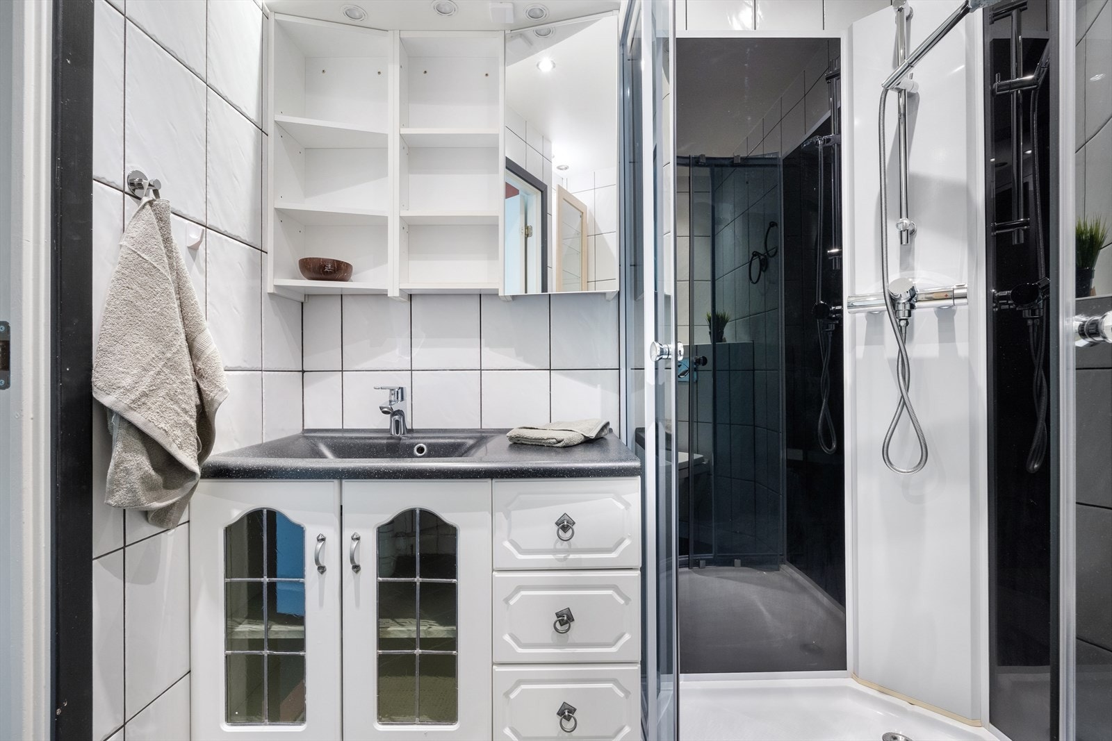 Badet er innredet med dusjkabinett, vegghengt toalett, benkeskap med nedfelt servant og speil med belysning over. Galleribilde