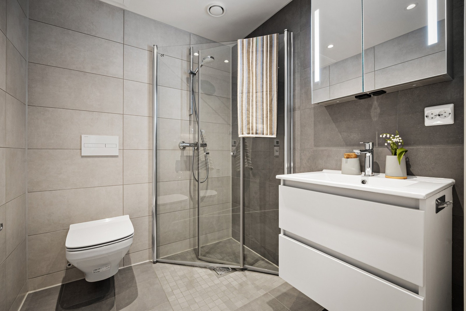 Pent servantskap med skuffer, hvit benkeplate og servant, veggmontert speil med innfelt lys. Vannbåren varme i gulv. Galleribilde