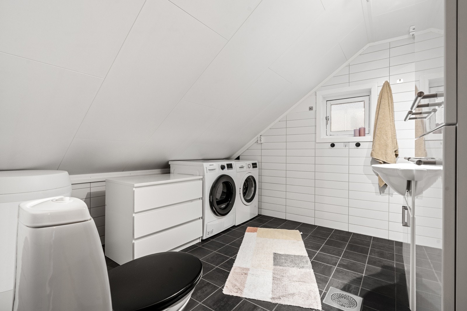 Badet er flislagt og fremstår pent og romslig med dusjhjørne, gulvmontert wc, servant, opplegg for vaskemaskin og rikelig med skapplass. Galleribilde