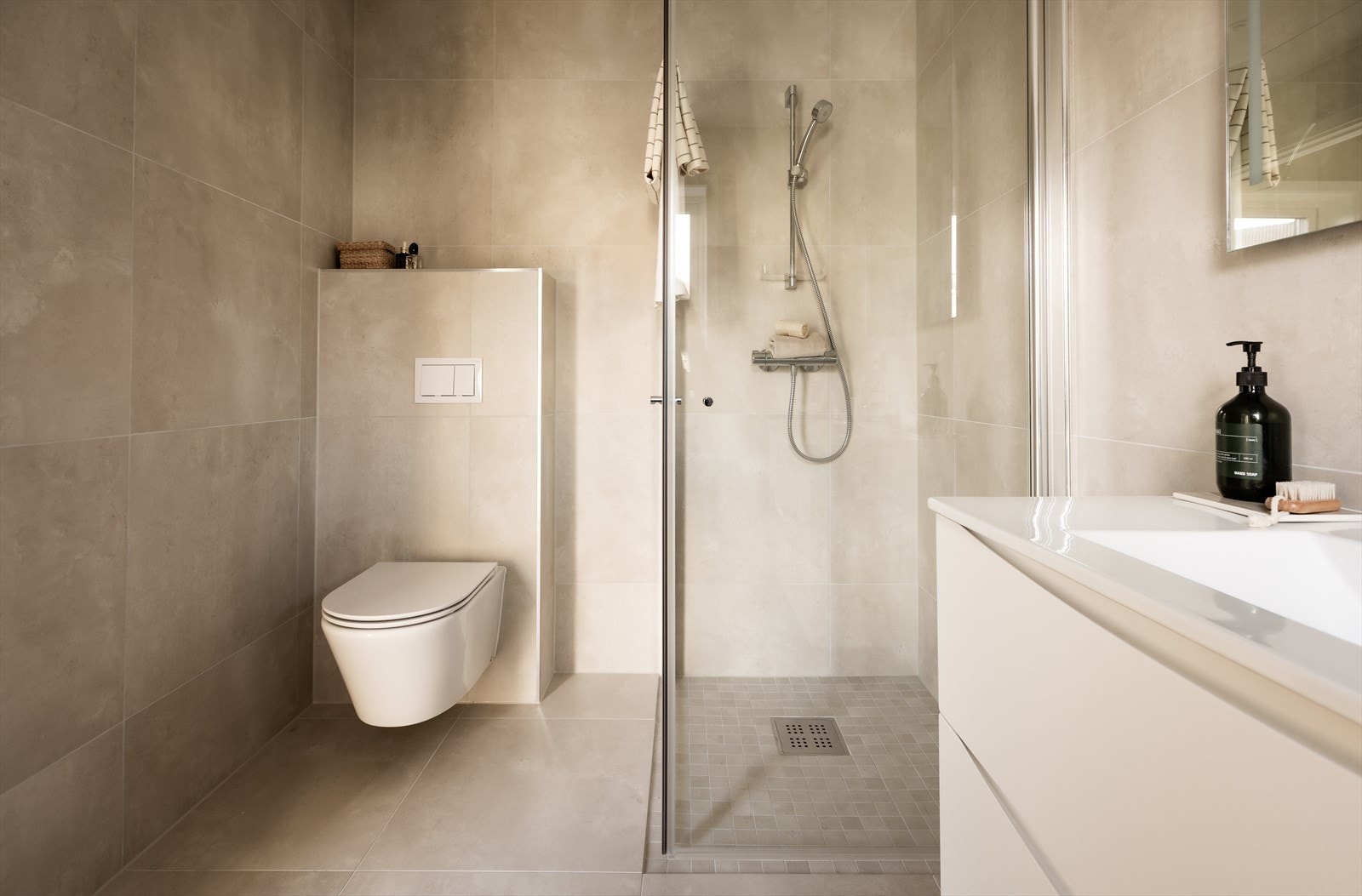 Badet er utstyrt med et servantskap med skuffer og en heldekkende servant med ettgreps blandebatteri. Over servanten er det et speil med integrert lys. Badet har også et vegghengt toalett og et dusjhjørne med glassdører. Galleribilde