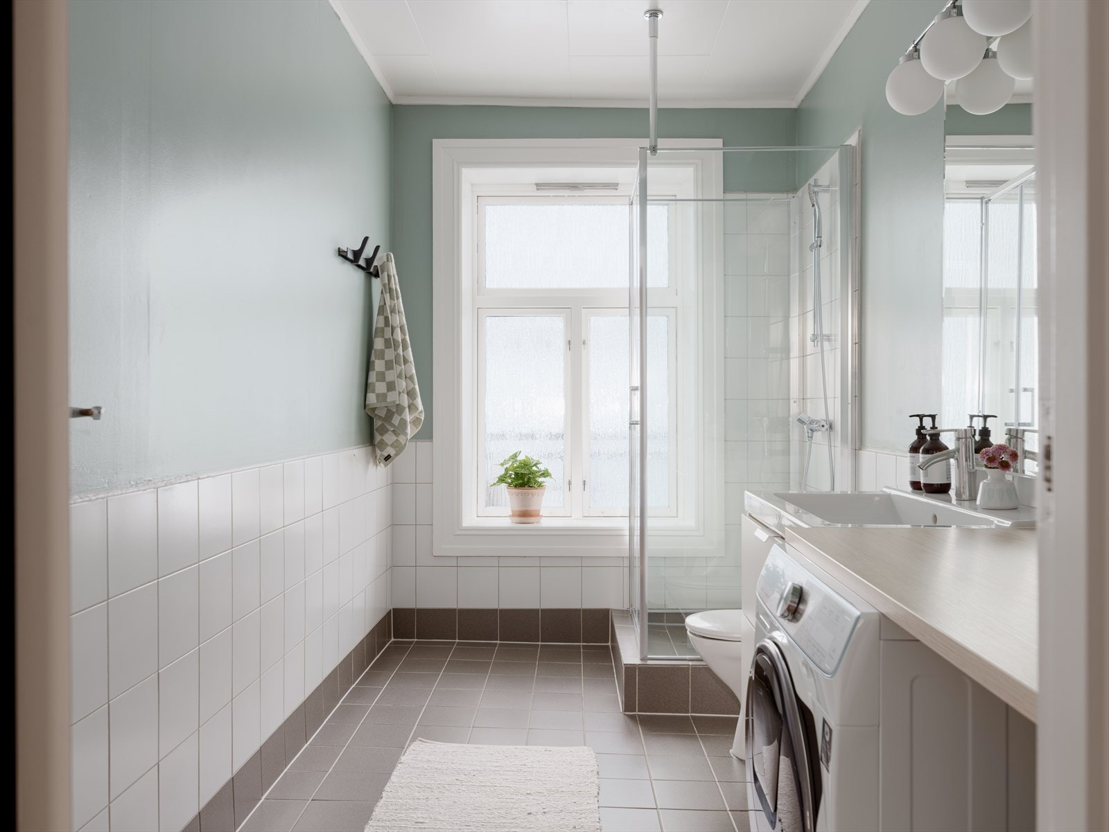 Rommet har dusjhjørne med svingbare glassdører, toalett og en heldekkende servant med speil og lysarmatur. Galleribilde