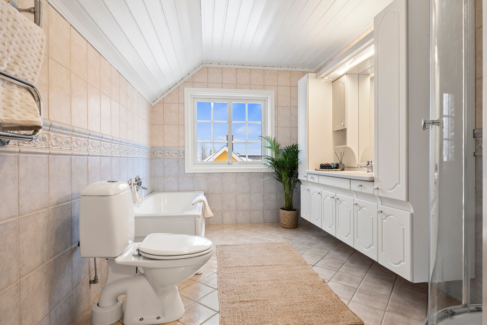 Stort og lyst bad med vindu. Servant integrert i lys skapinnredning med speil og lys, wc, badekar og dusjkabinett. Galleribilde