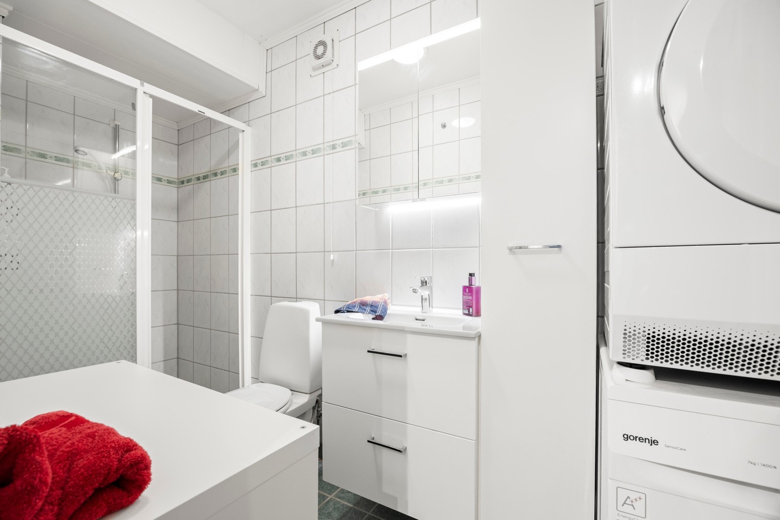 Bad i hybel har flislagte vegger og gulv med varmekabler. Servant i lys skuffeinnredning, speilskap med lys, dusjnisje og wc. Det er opplegg for vaskemaskin og tørketrommel. Galleribilde