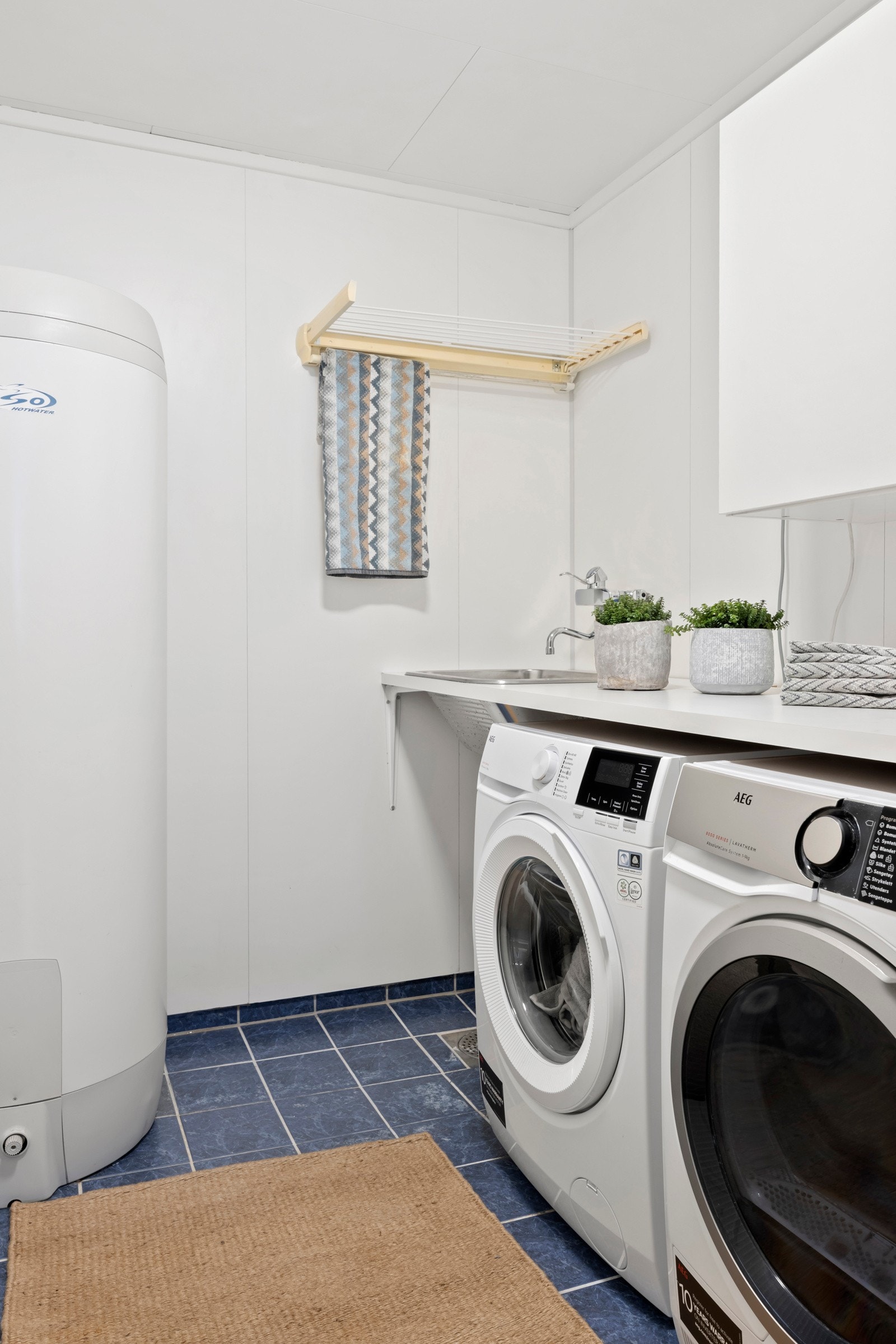 Vaskerom med flislagt gulv med varmekabler, baderomspanel på vegger med innredning, skyllekum og opplegg for vaskemaskin og tørketrommel. Galleribilde