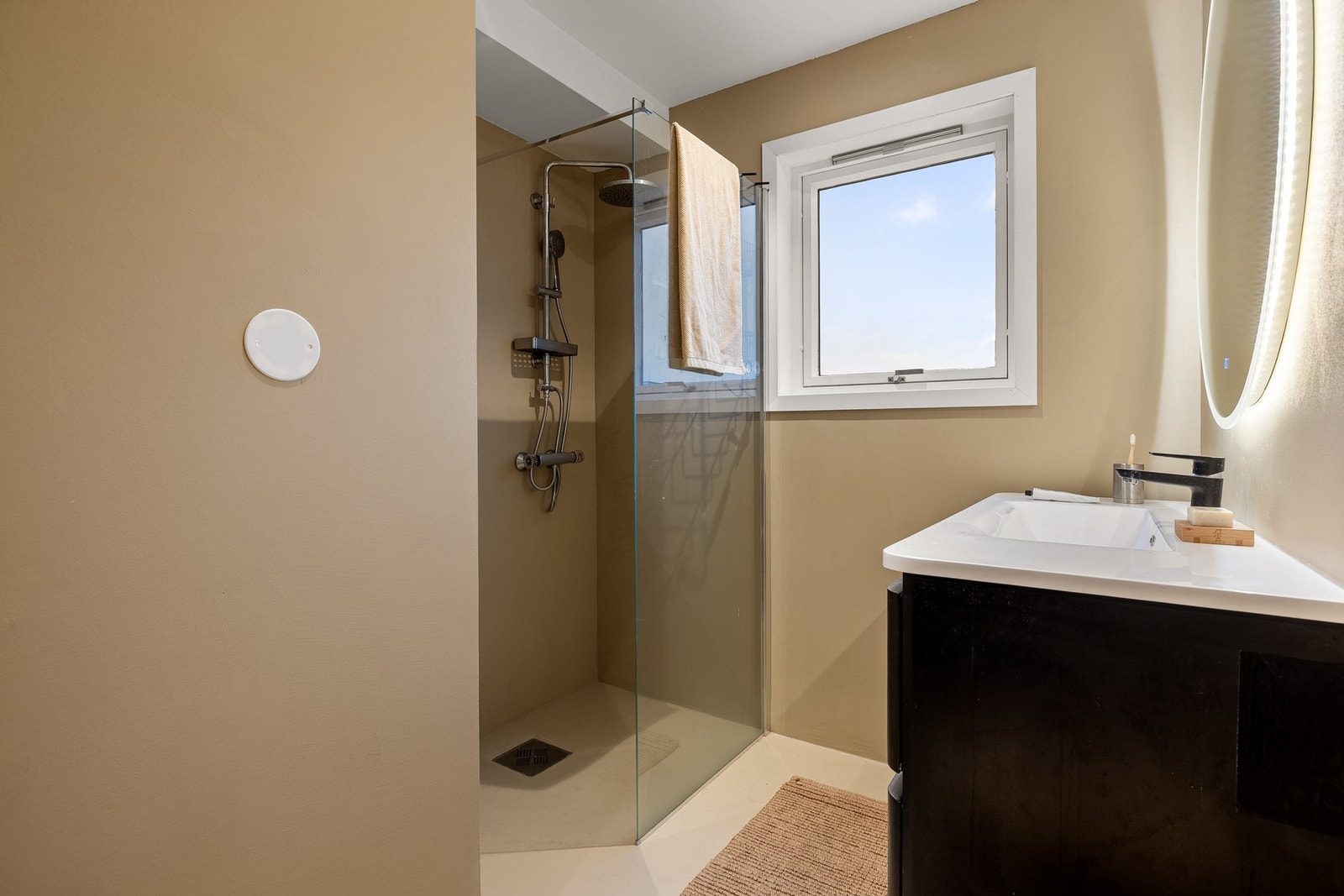 Badet er innredet med vegghengt toalett, servant med innredning og dusjhjørne. Galleribilde