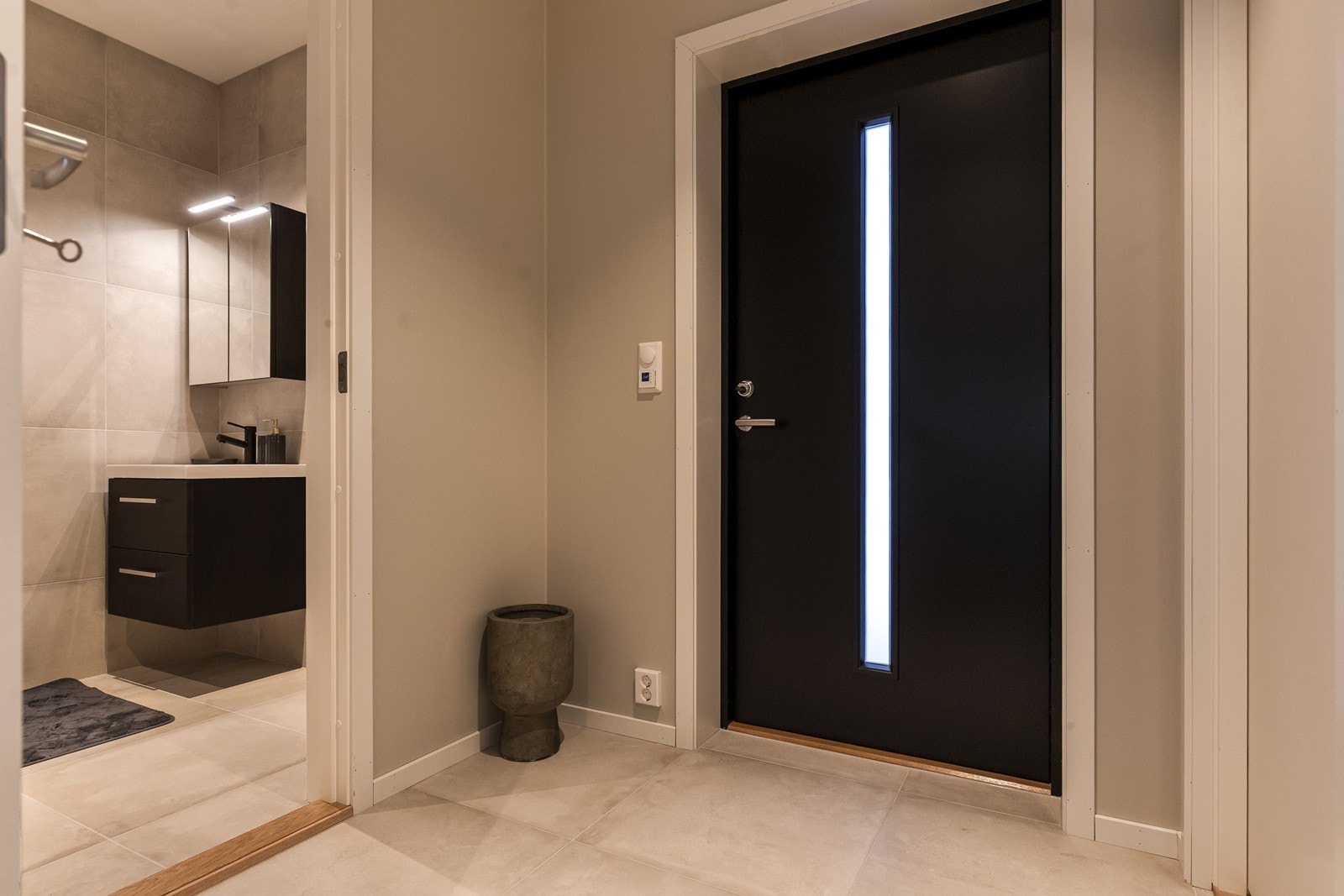 Velkommen inn i en lys entré med direkte tilgang til et av boligens to bad. Fra entreen ledes du videre inn i boligens sosiale sone. (Bilde fra speilvendt bolig). Galleribilde