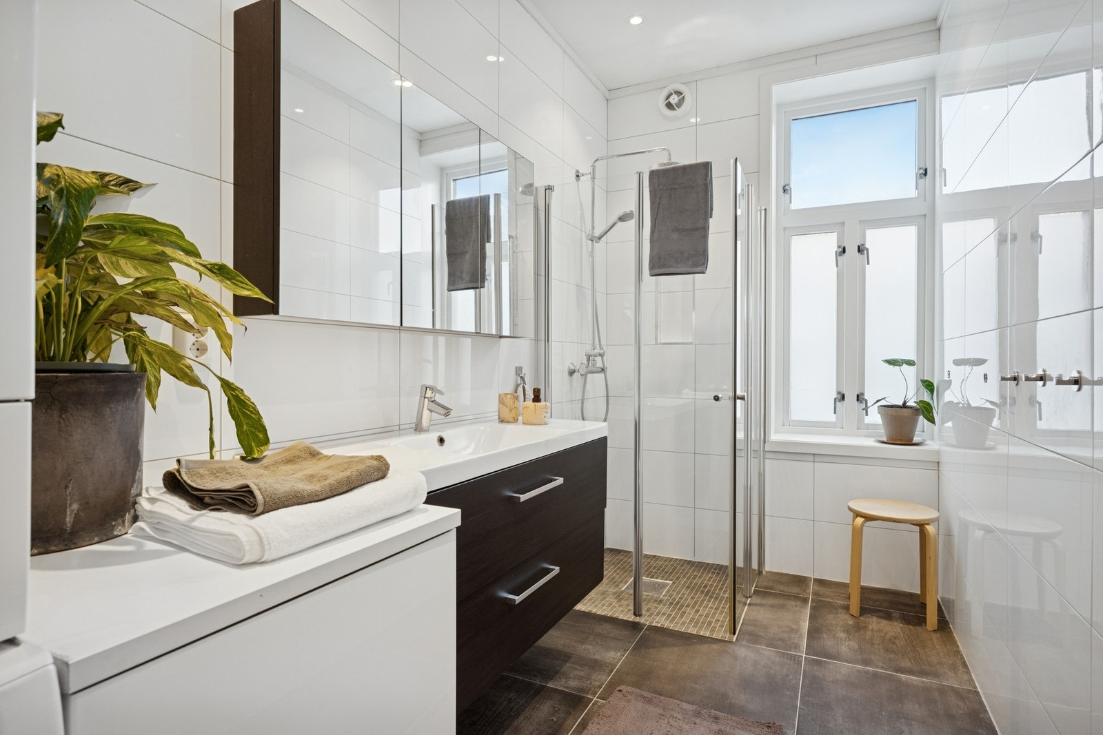 Delikat bad med romslig dusjløsning og glassvegger. Store flislagte flater og vindu gir et lyst og behagelig uttrykk. Galleribilde