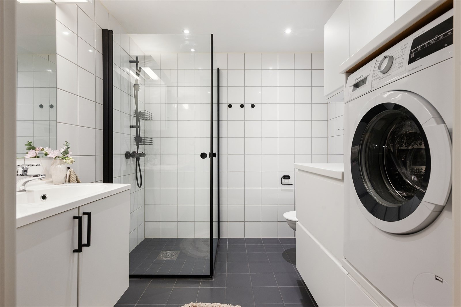 Romslig og pent baderom med vegghengt toalett, servant nedfelt i innredning, speilskap og dusjhjørne med svingbare glassdører. Galleribilde