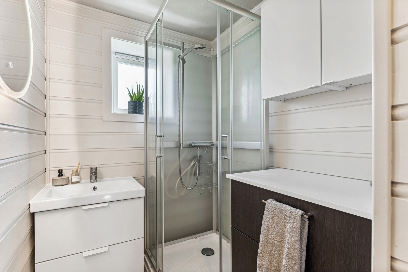 Baderommet har et praktisk dusjkabinett og en nyere servant og innredning fra Ikea samt speil med led-belysning. Galleribilde