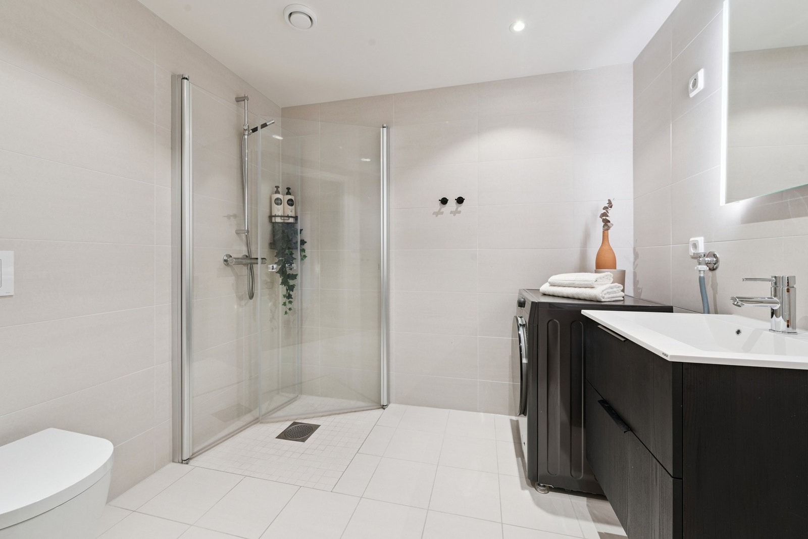 Delikat flislagt bad med dusjhjørne, moderne innredning og opplegg for vaskemaskin. Galleribilde