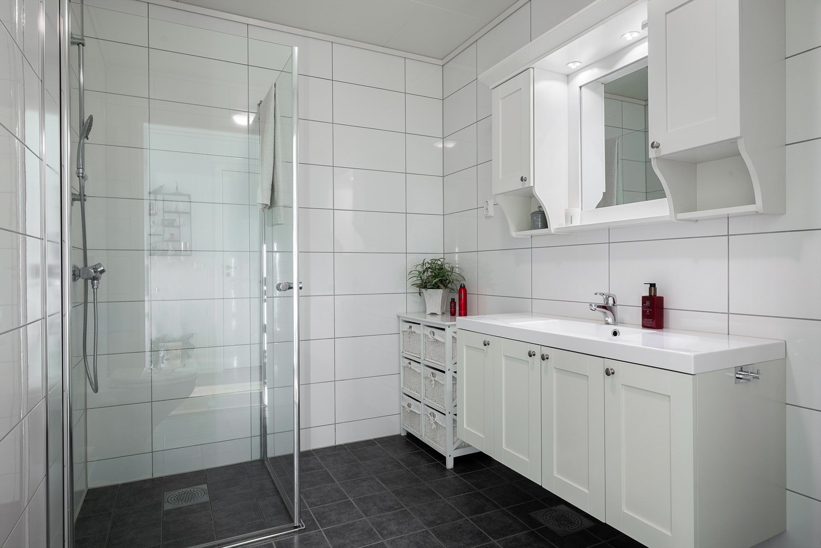 Lyst og tidløst baderom utstyrt med dusjhjørne, servantinnredning og toalett. Galleribilde