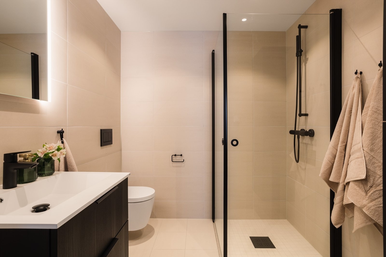 Badet er utført i en tidløst stil, med flislagte gulv og vegger. Innredningen består av et vegghengt toalett, dusjhjørne, servant og speil med belysning. Galleribilde