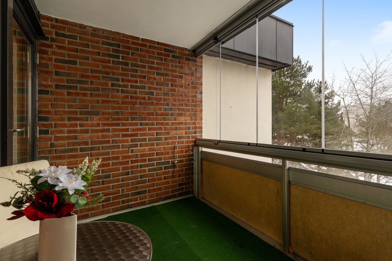 Flott innglasset balkong med betonggulv og vegger av glass og mur. Galleribilde