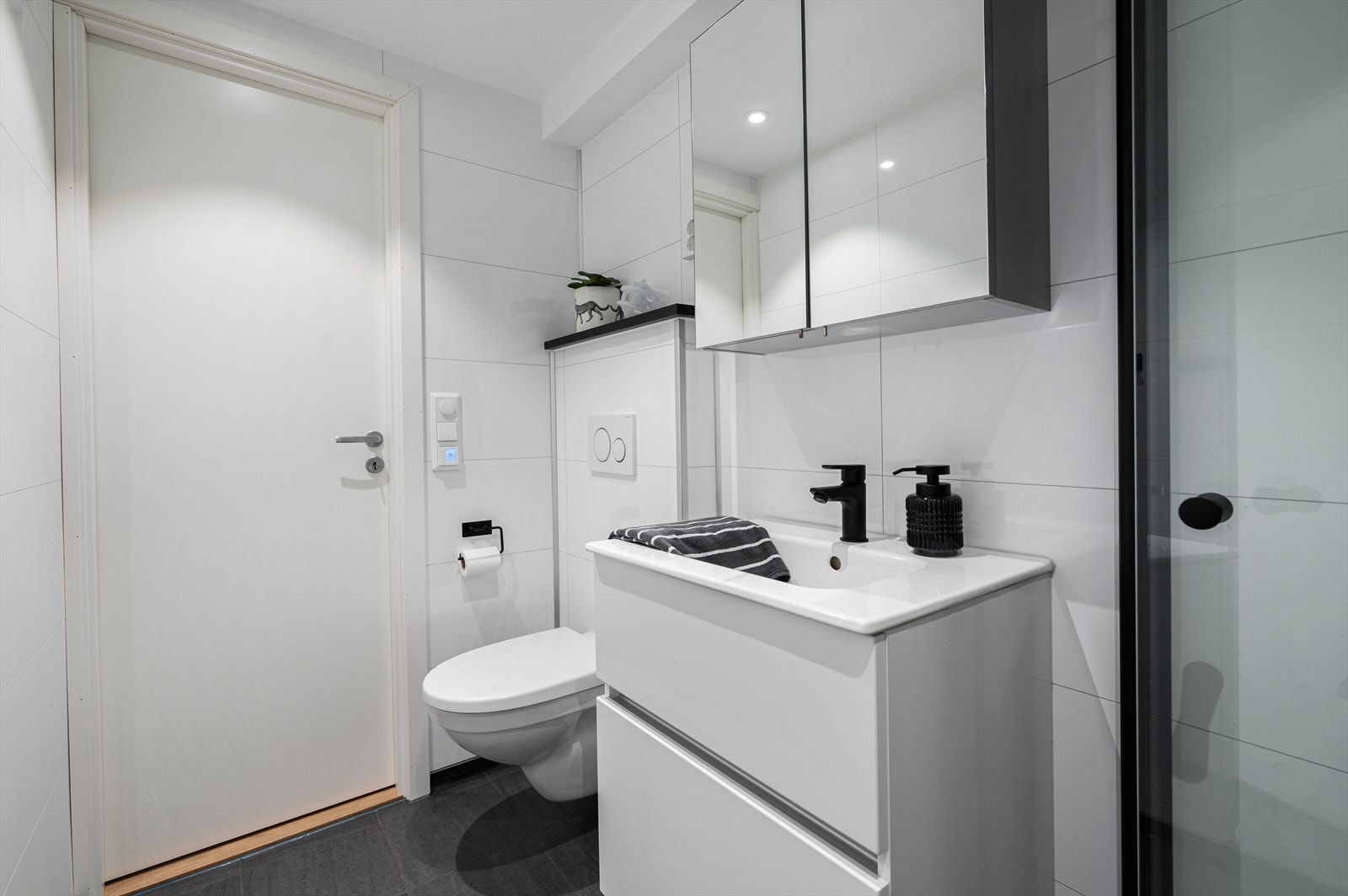 Badet er utstyrt med dusjnisje, mekanisk avtrekk, servant, servantskap og veggmontert wc. Galleribilde