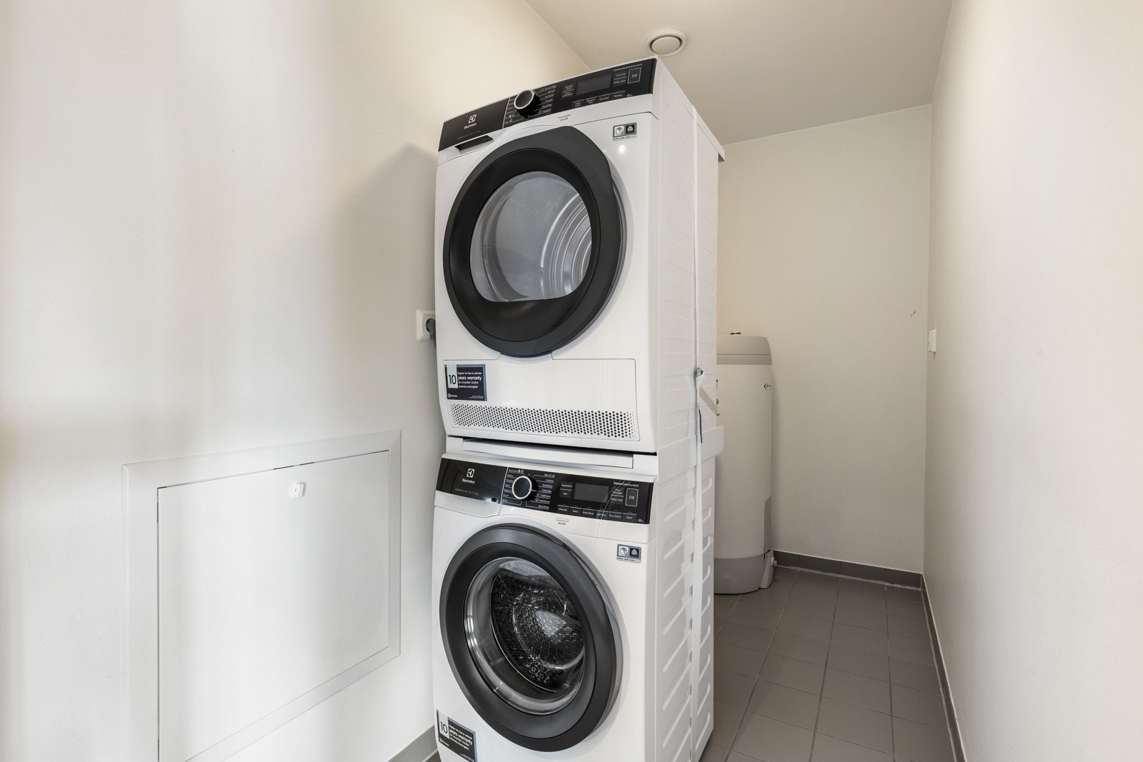 Vaskerom med opplegg for vaskemaskin og tørketrommel, flislagt gulv og lysmalte vegger. Galleribilde