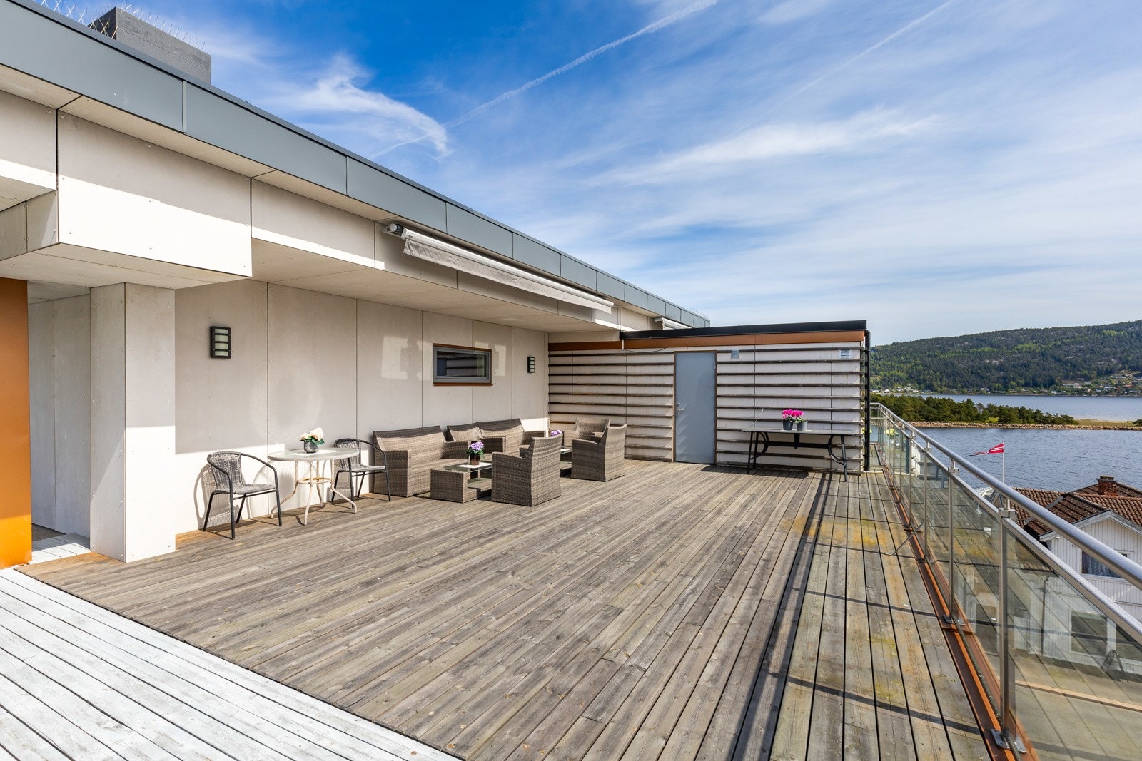 Stor felles terrasse med sittegruppe og utsikt mot vannet og åsene. Galleribilde