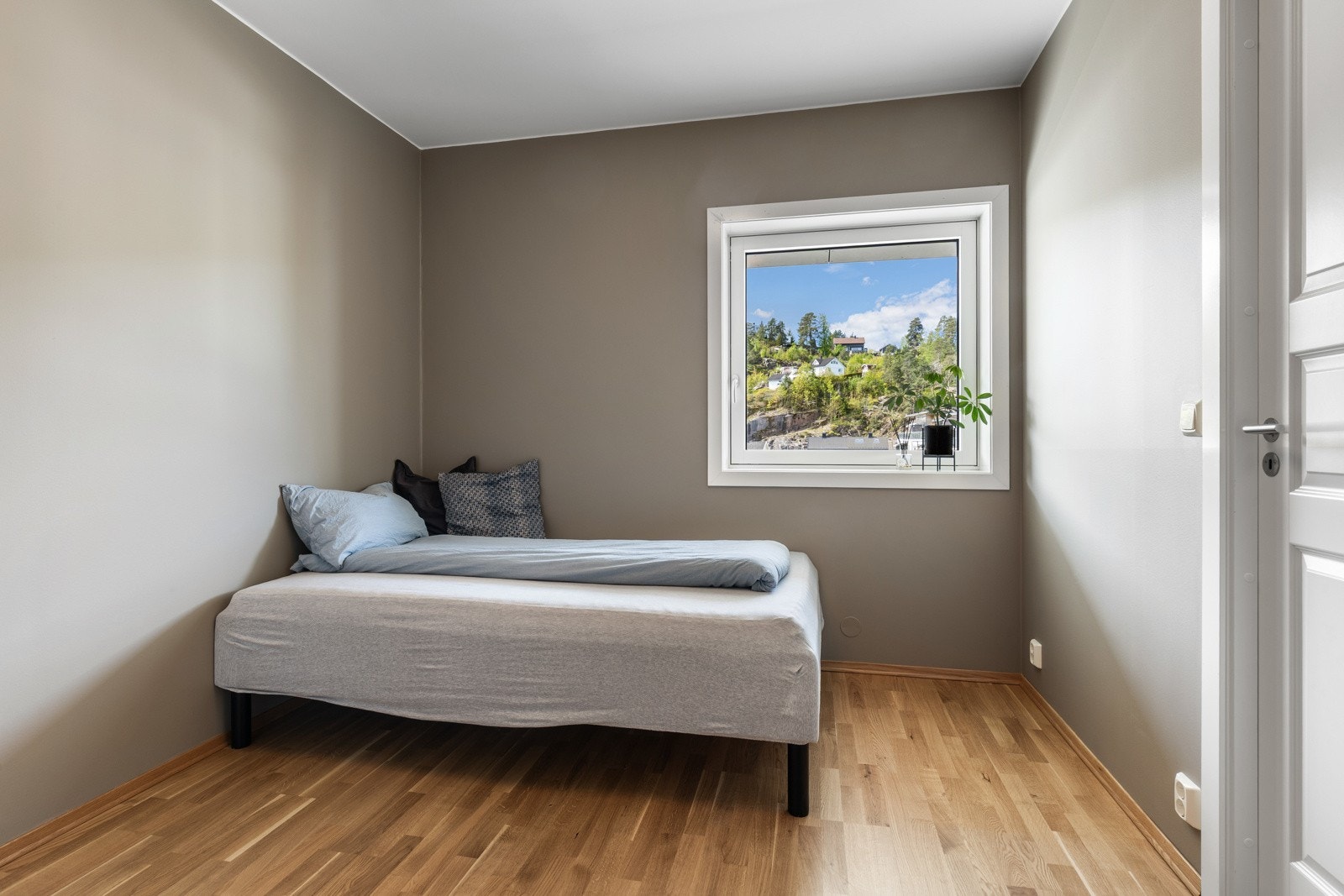 Soverom med parkettgulv, grå vegger og stort vindu som gir naturlig lys. Galleribilde