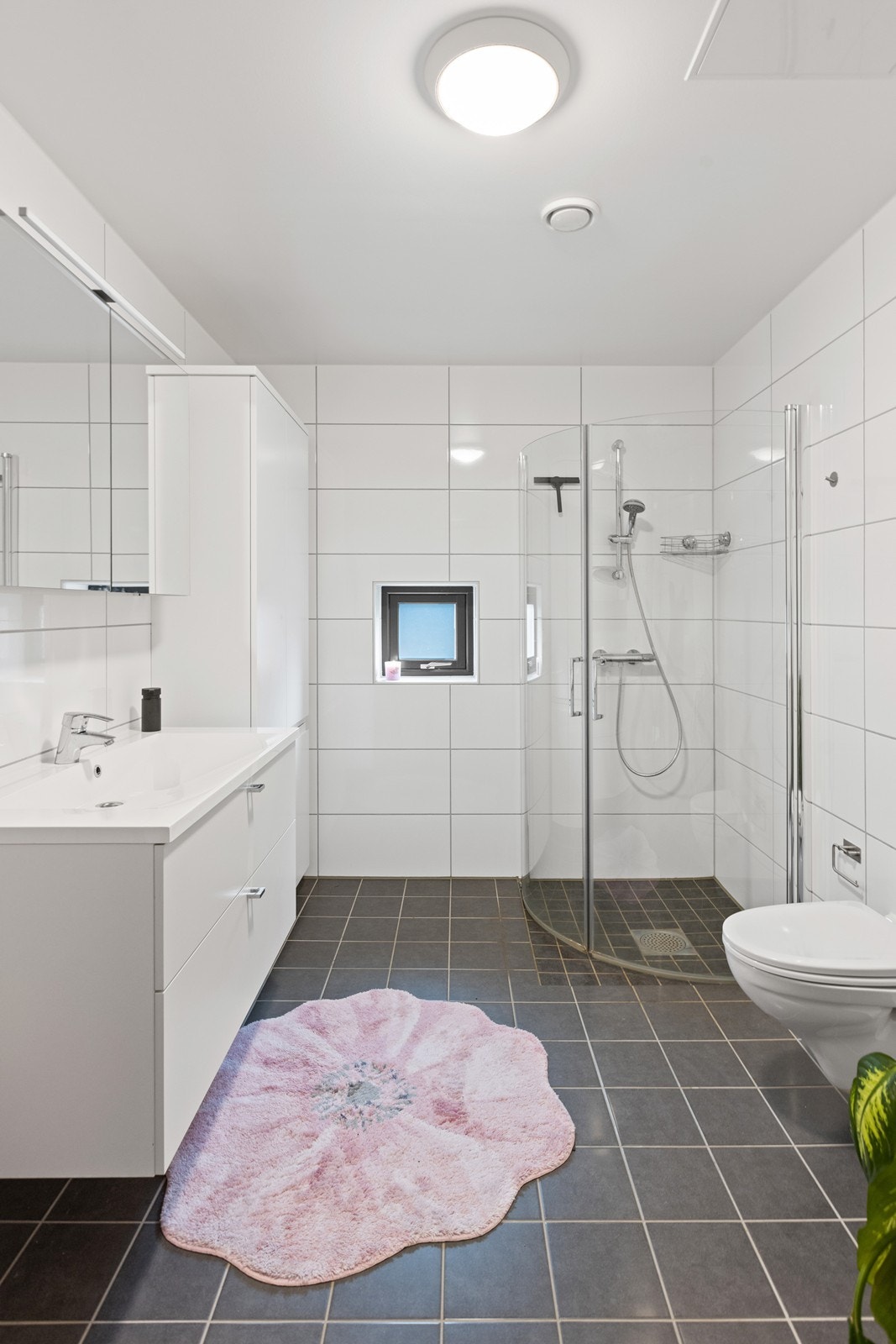 Dusjhjørne med glassvegger, vegghengt toalett og servant med innredning. Galleribilde