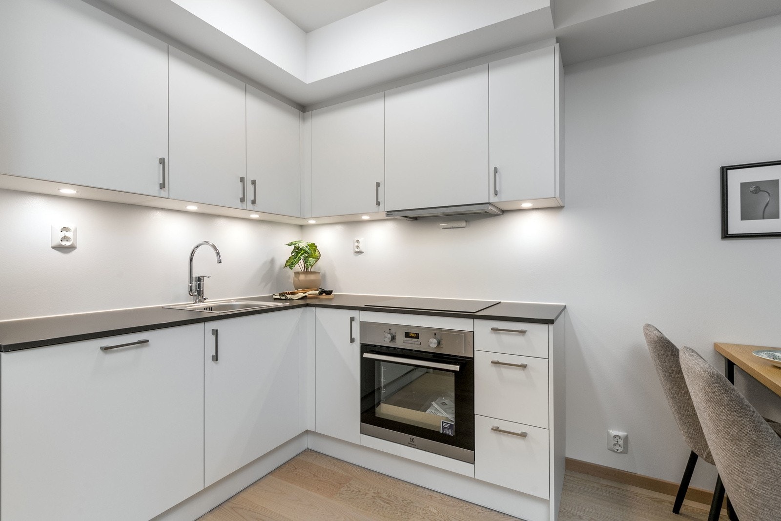 Lekkert kjøkken i åpen løsning mot stue, med integrerte hvitevarer. Kjøkkenet har en praktisk hjørneløsning, som gir rikelig av skap og benkeplass. Bilde fra L406. Galleribilde