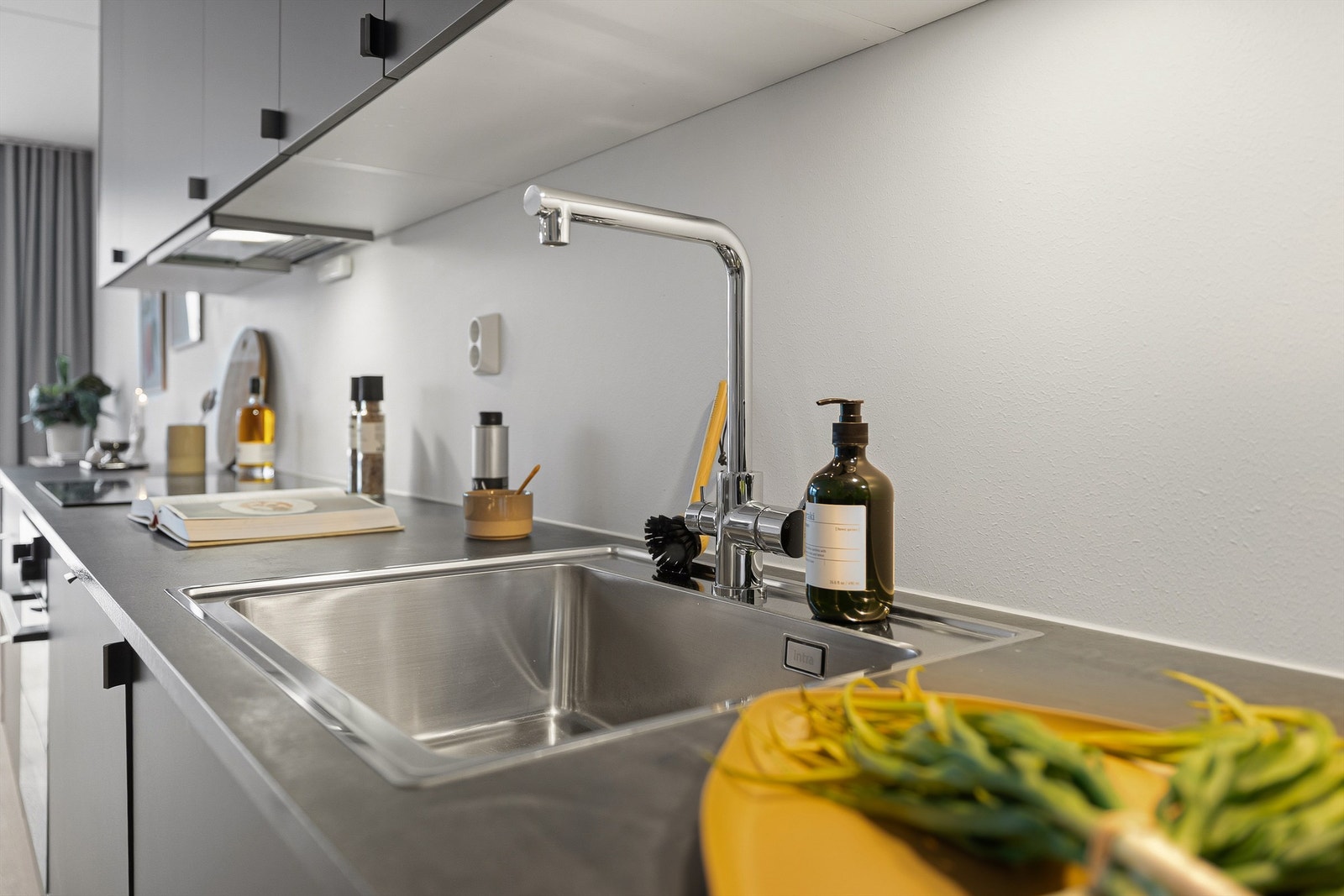 Nedfelt oppvaskkum med to-greps kjøkkenarmatur og stikkontakter over benkeplater. Galleribilde